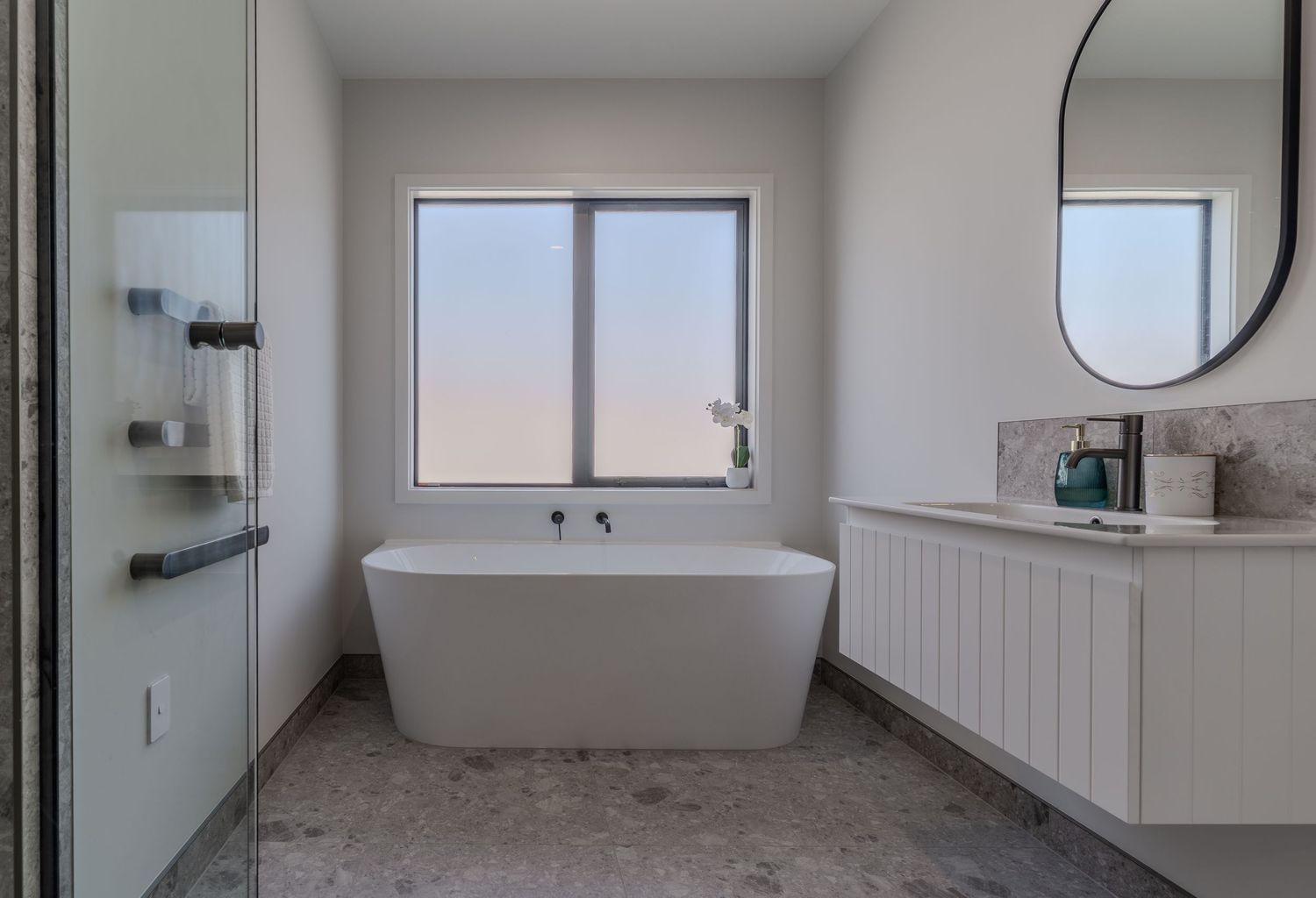 Modern bathroom with freestanding soaking tub, floating vanity, round mirror, and large window with scenic views.