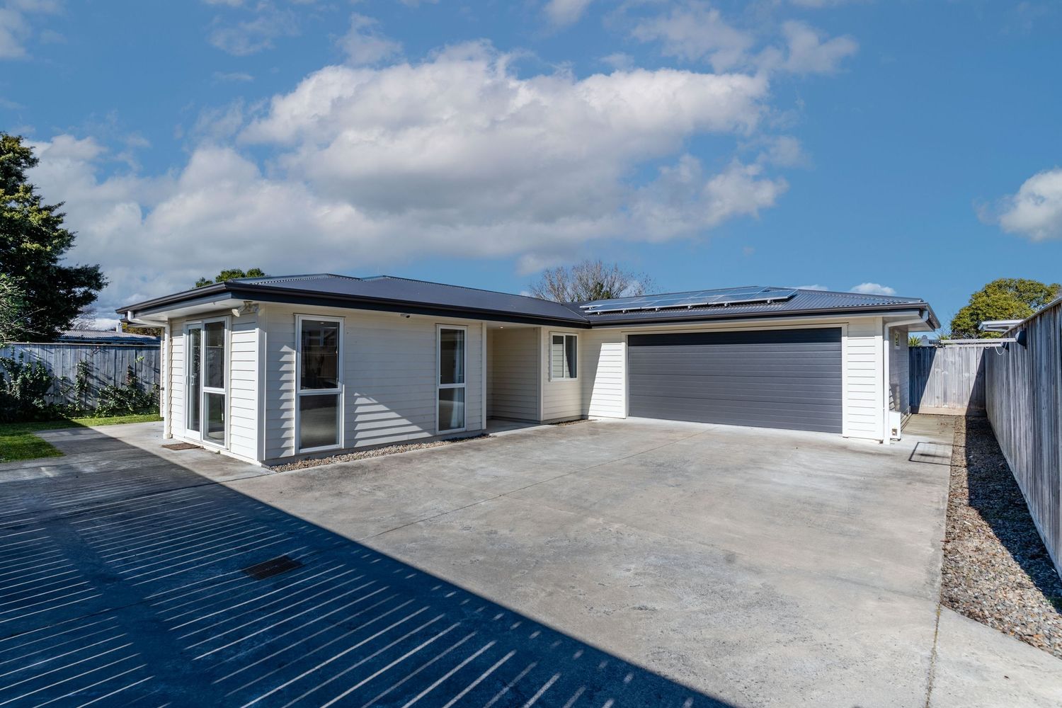 New Zealand residential home featuring solar panels, double garage, and spacious concrete driveway.