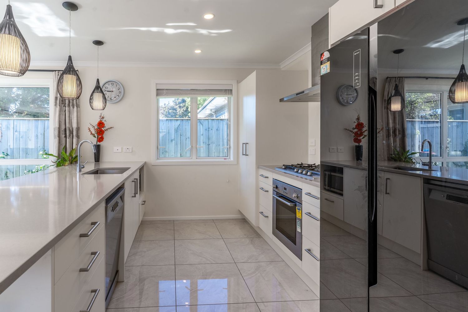 Sleek white kitchen with tile floors, gas stove, stainless dishwasher, and garden views through dual windows.