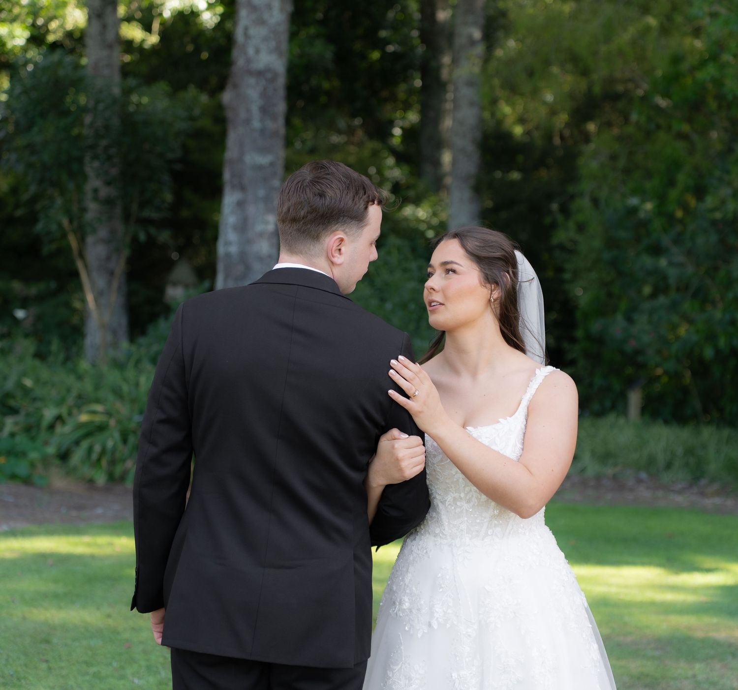 Bride and groom sharing a tender first look moment in a lush green garden setting.