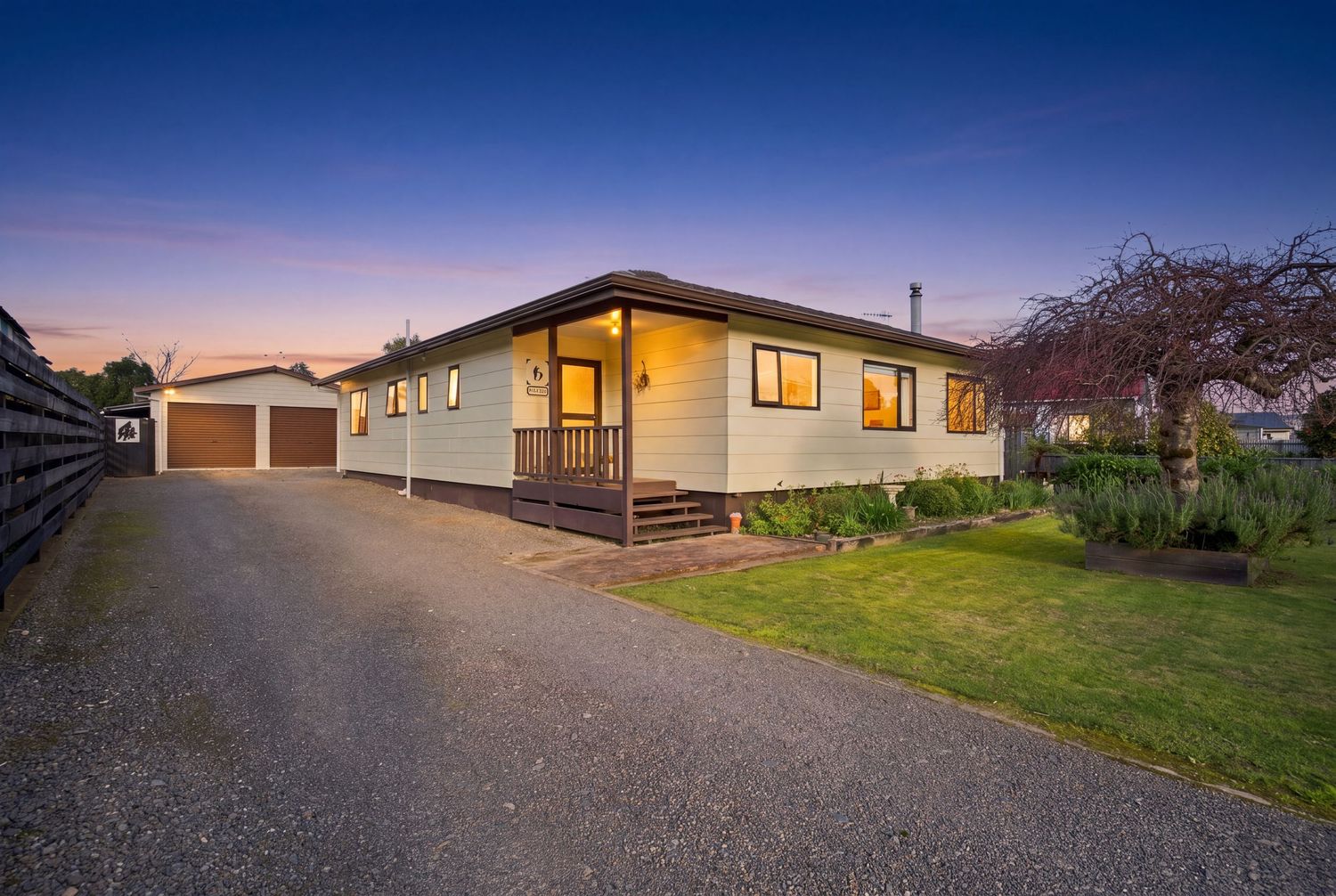 A charming single-story home with a double garage, driveway, and lush lawn photographed at dusk with warm interior lighting.