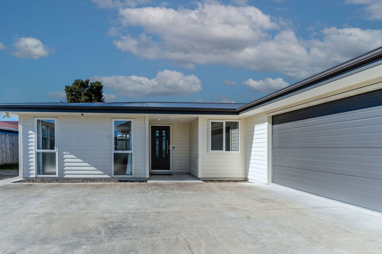 Modern single-story home with cream weatherboard cladding, solar panels, and double garage under blue skies.