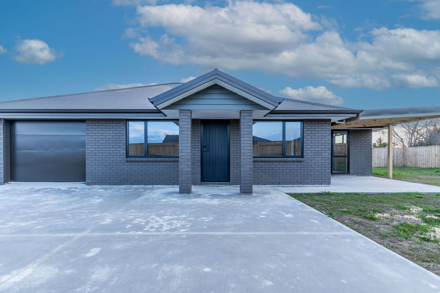 New build brick house featuring double garage and dark front door on concrete driveway.