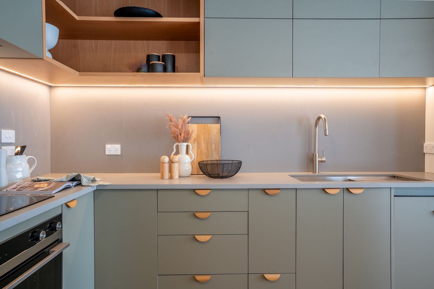 Modern sage green kitchen with timber accents, under-cabinet lighting, and integrated appliances.