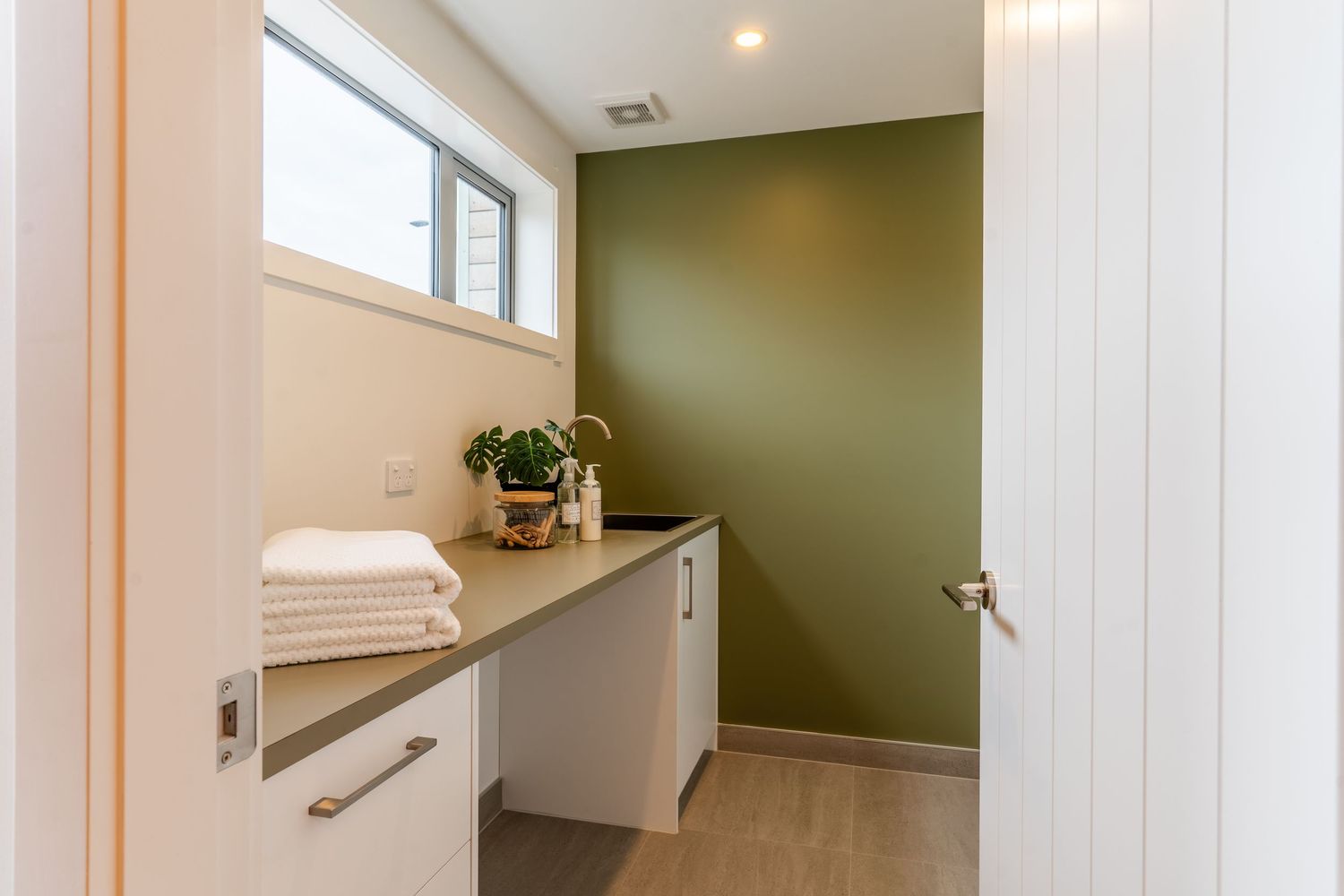 Compact laundry room with olive green accent wall, white cabinetry, and folded towels.