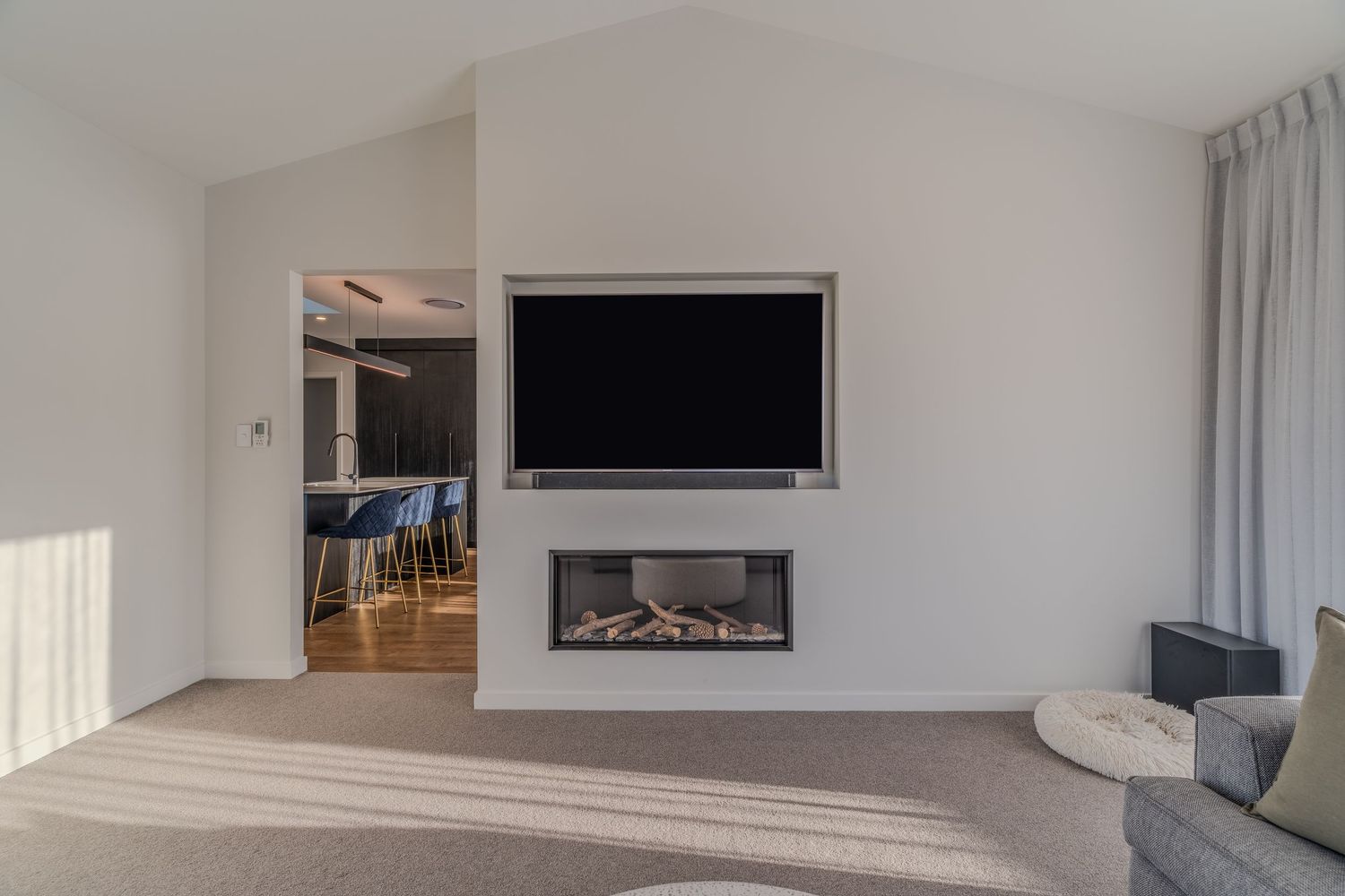 Modern living room with built-in fireplace, wall-mounted TV, and neutral carpet flooring with vaulted ceilings.