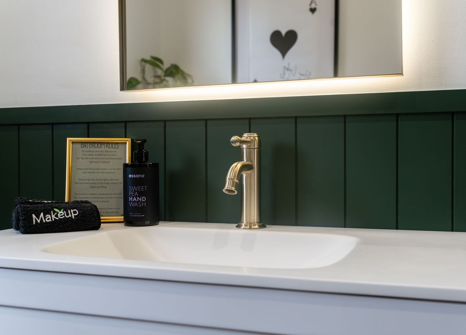 Modern bathroom vanity with gold faucet, green paneling, white sink, and makeup bag on counter.