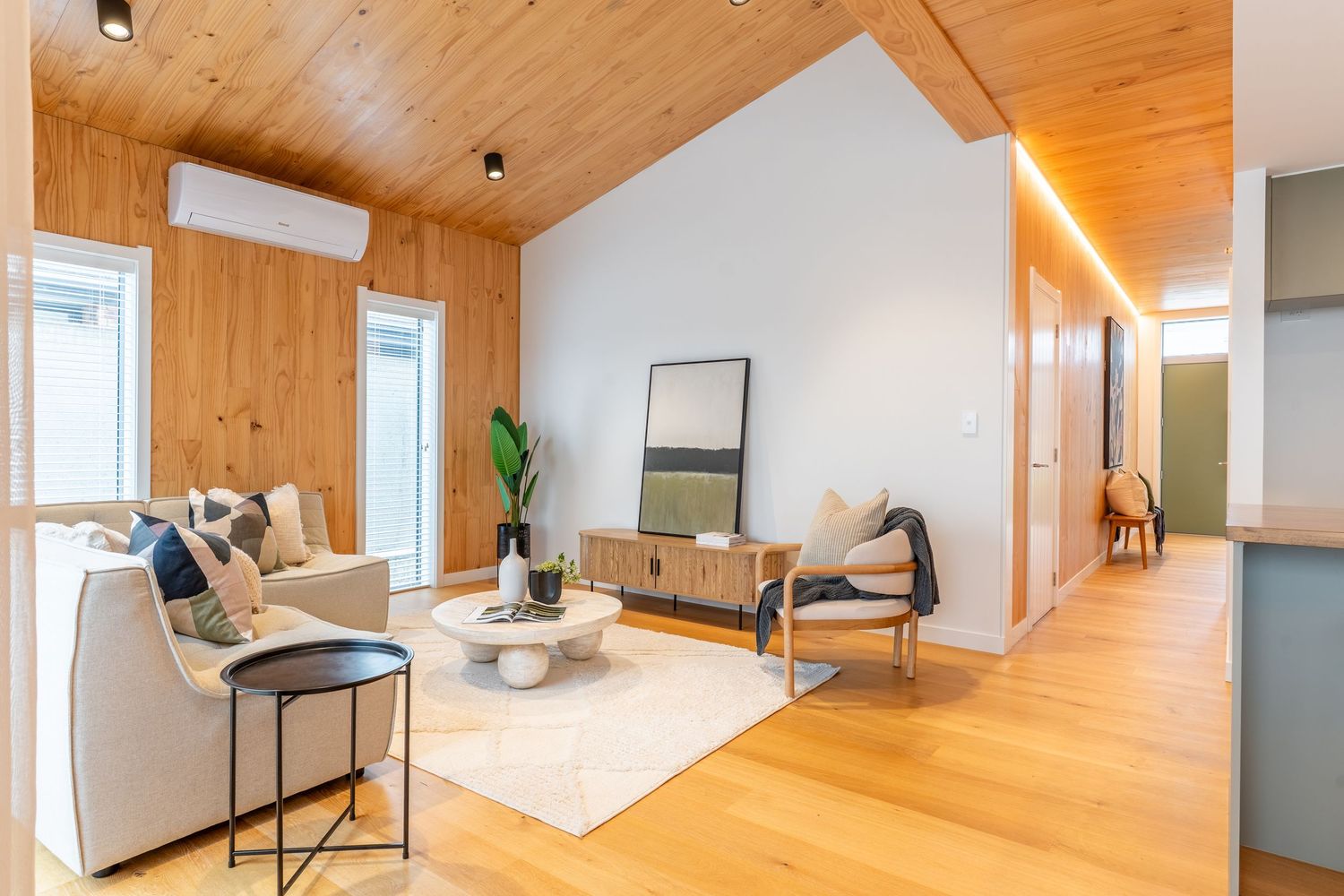 Stylish living room with wood-paneled walls, vaulted ceiling, light hardwood floors, and modern furniture arrangement.
