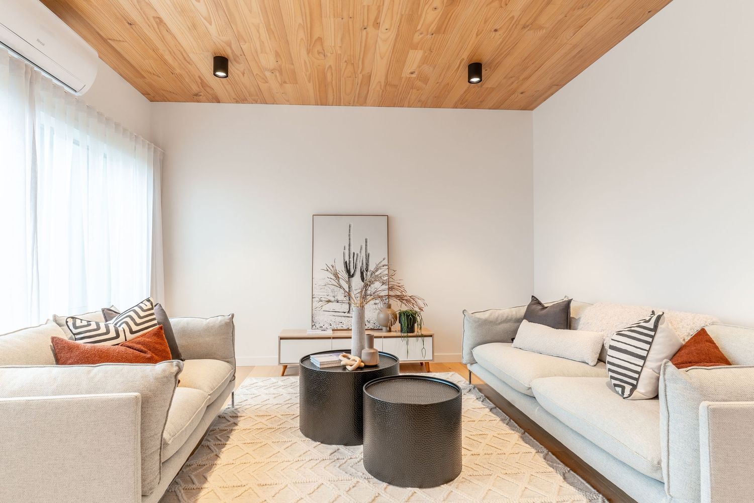 Stylish living room with timber ceiling, neutral sofas, and round black coffee tables.