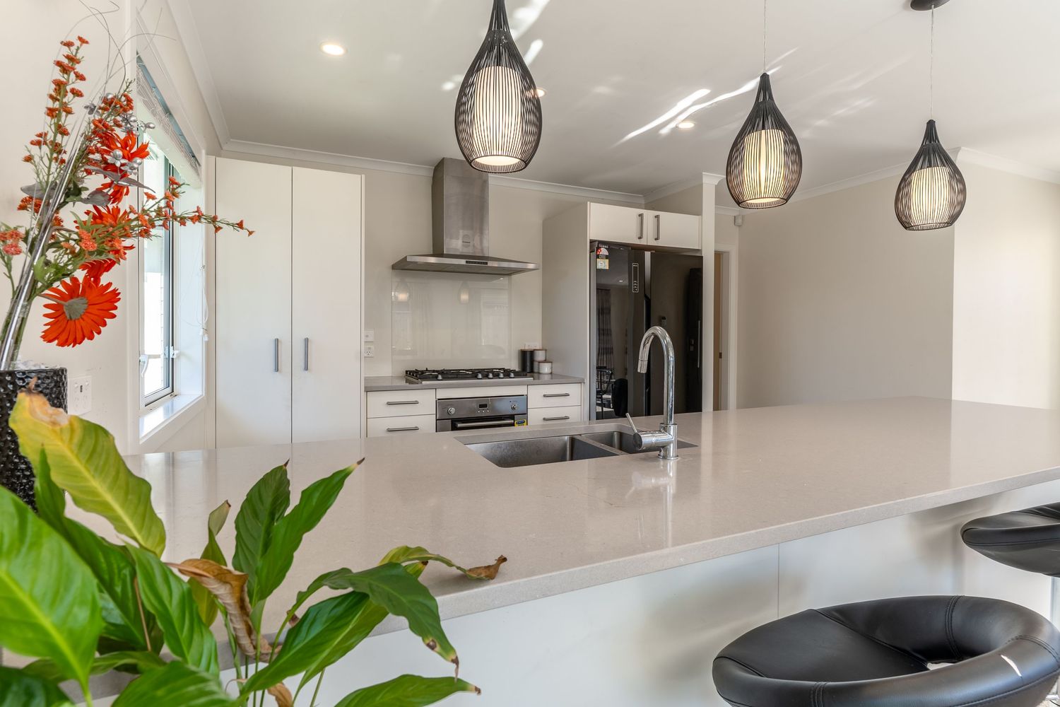 Contemporary white kitchen with large island, pendant lights, stainless appliances, and fresh floral arrangement.