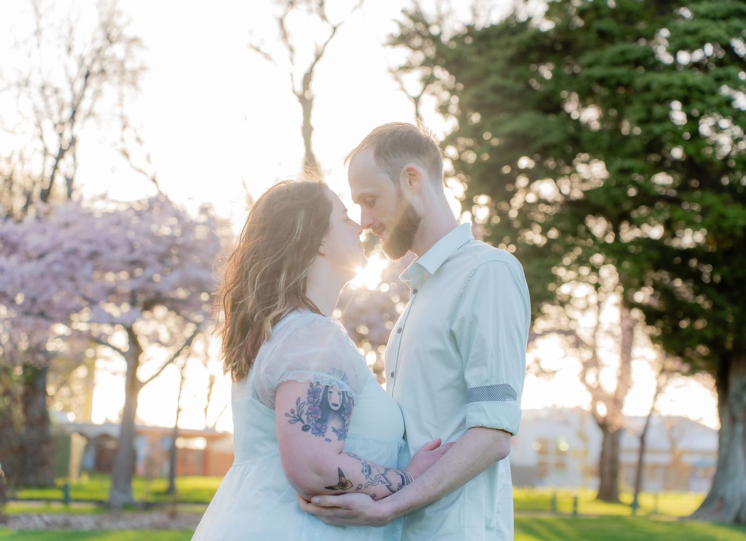 Expecting couple embracing at golden hour near blooming cherry blossom trees in a peaceful park.