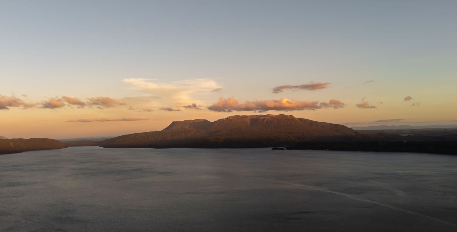 Aerial sunset view of calm water with large mountain silhouette on horizon.