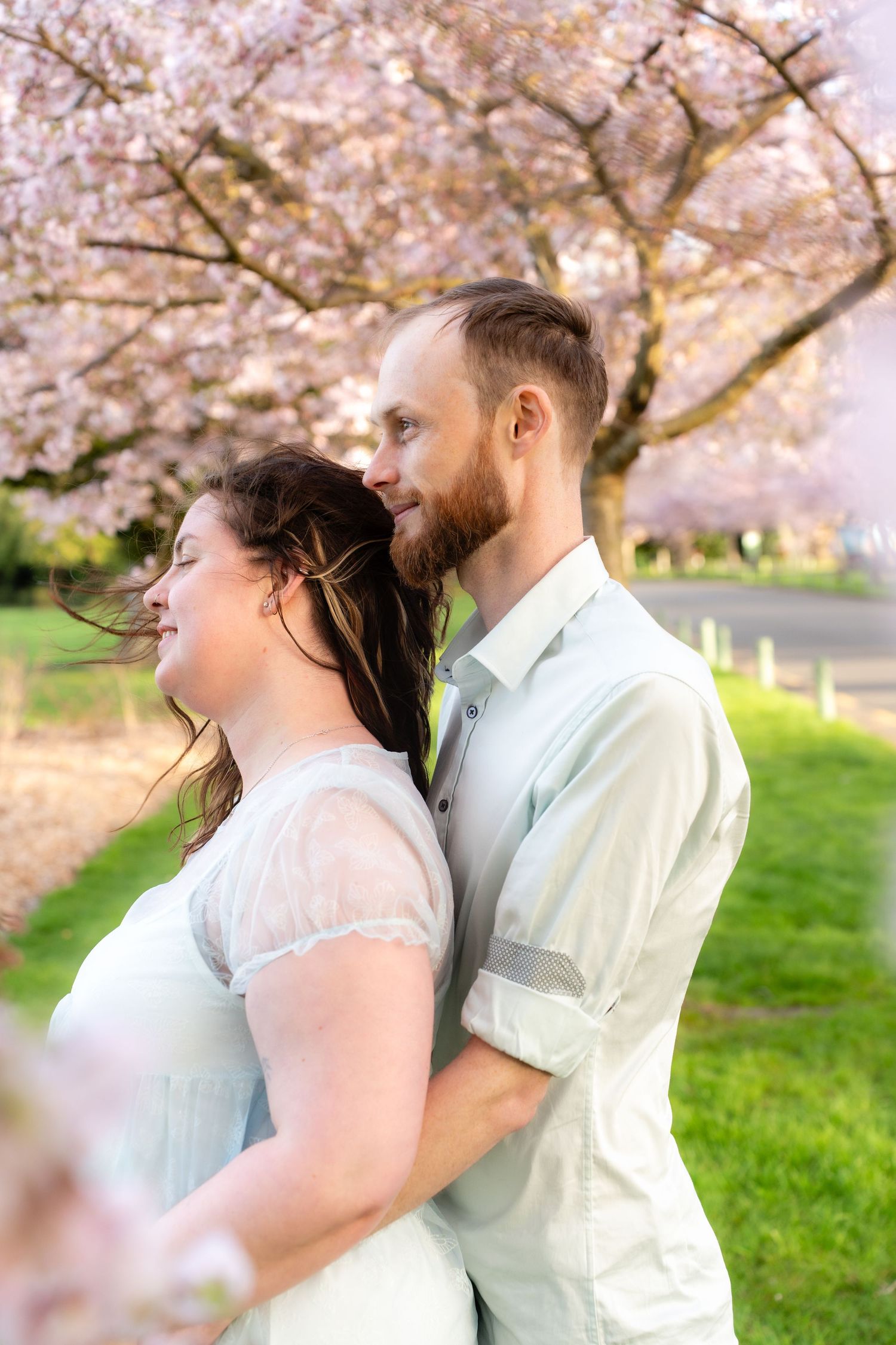 Romantic couple embracing under blooming pink cherry blossom trees on a sunny spring day.