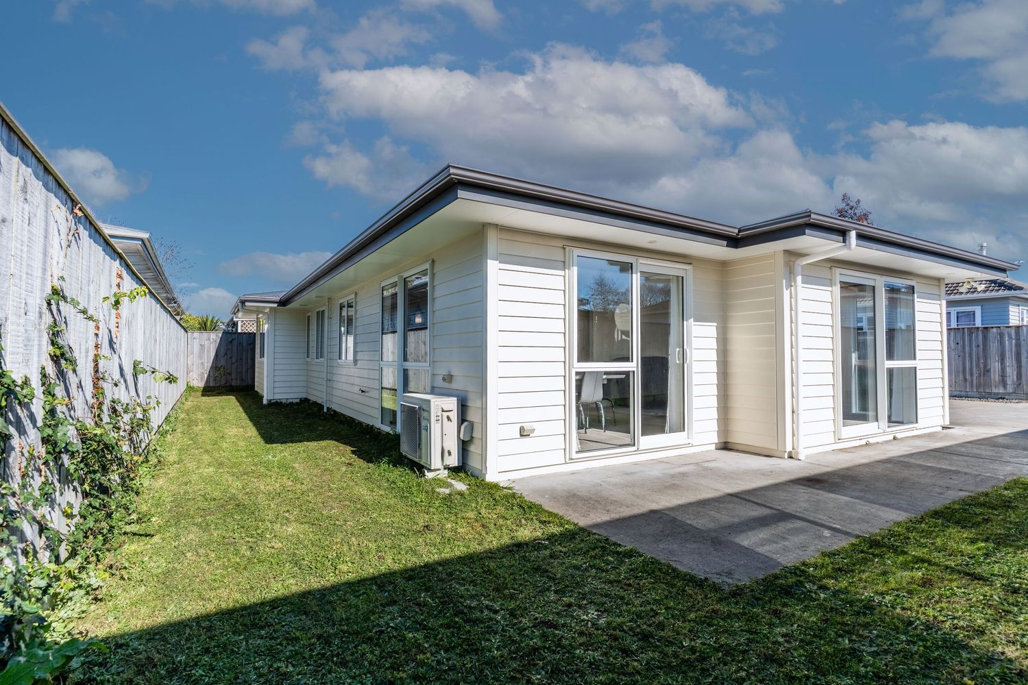 Side view of cream weatherboard home with large windows, patio, and well-maintained lawn.