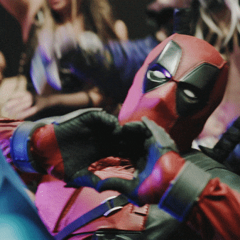 Person in a red and black Deadpool costume making a heart shape with their hands at a cosplay event.