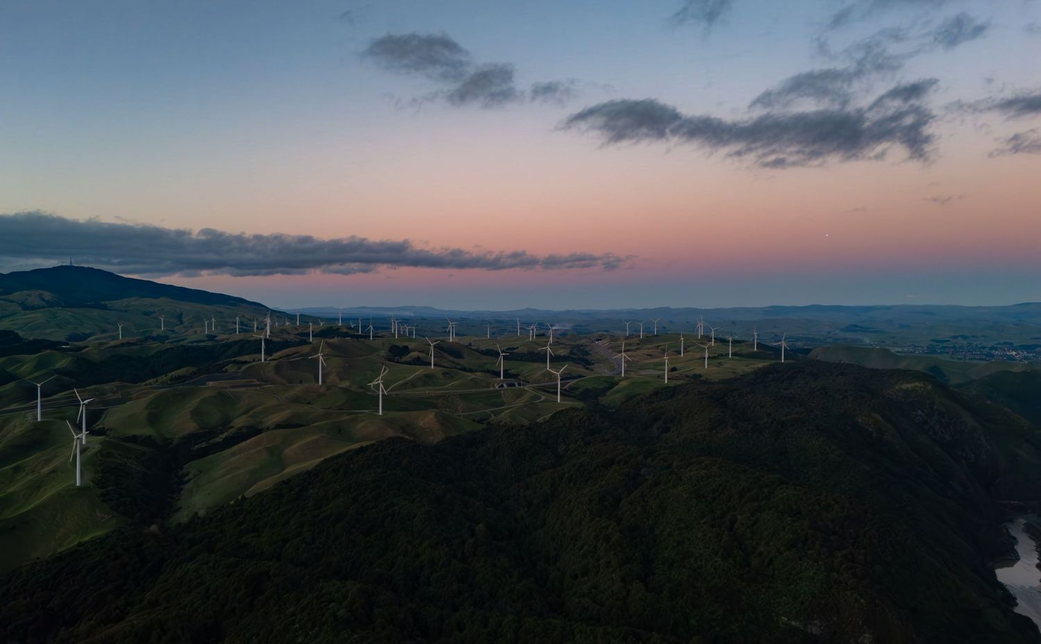 Aerial view of wind turbines on green rolling hills at sunset with pink and blue sky in ashhurst