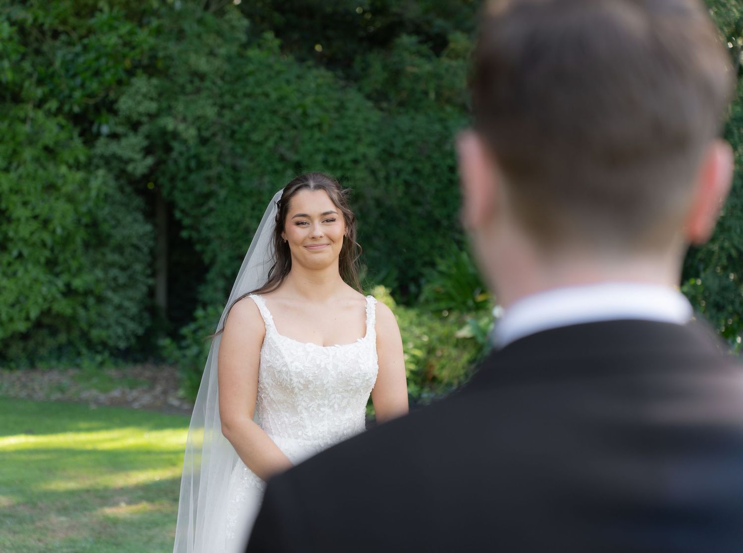 Smiling bride in white lace gown and veil during an emotional first look with groom.