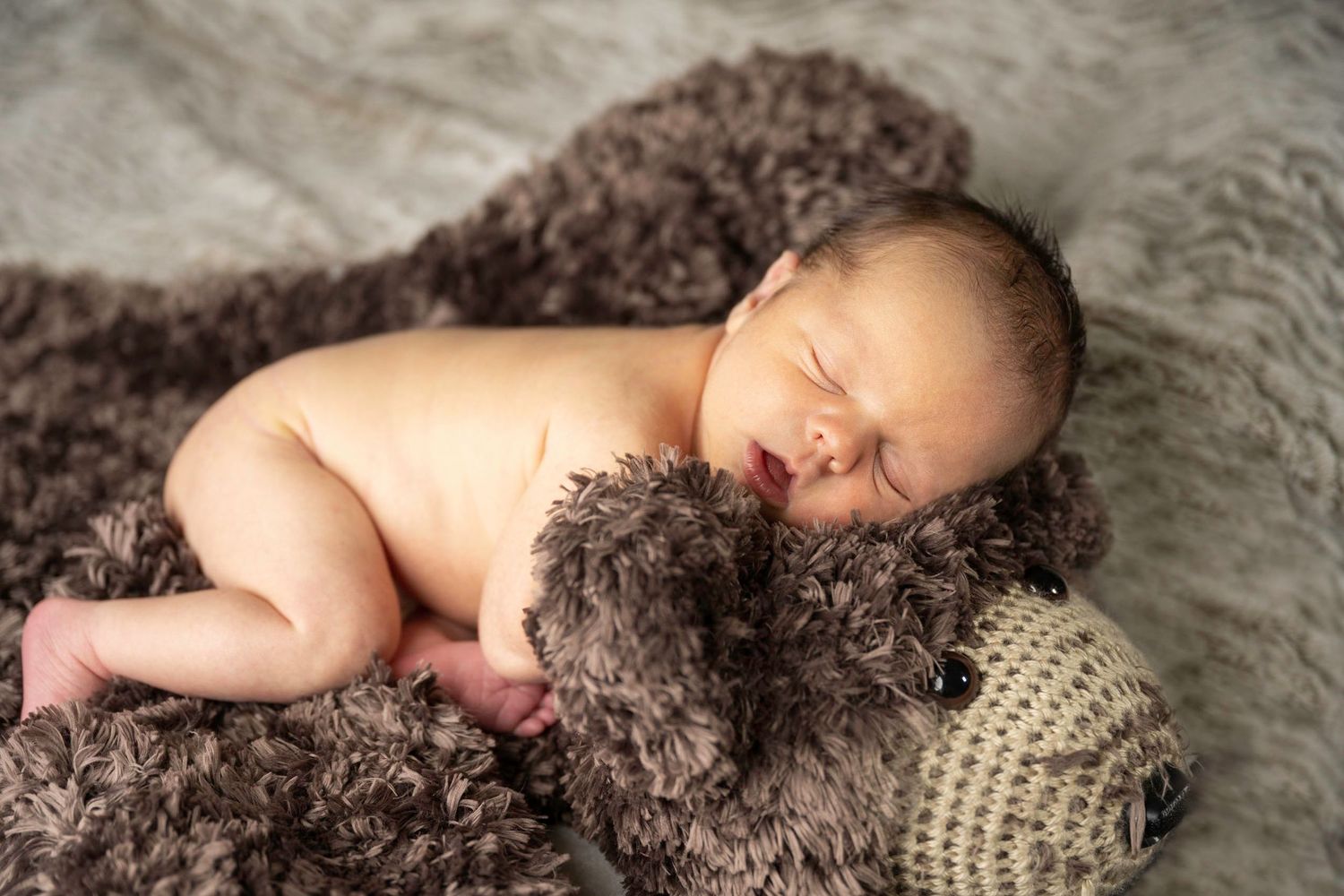 A five-day-old infant, newborn picture, cuddling on a comfy blanket with a stuffed bear head