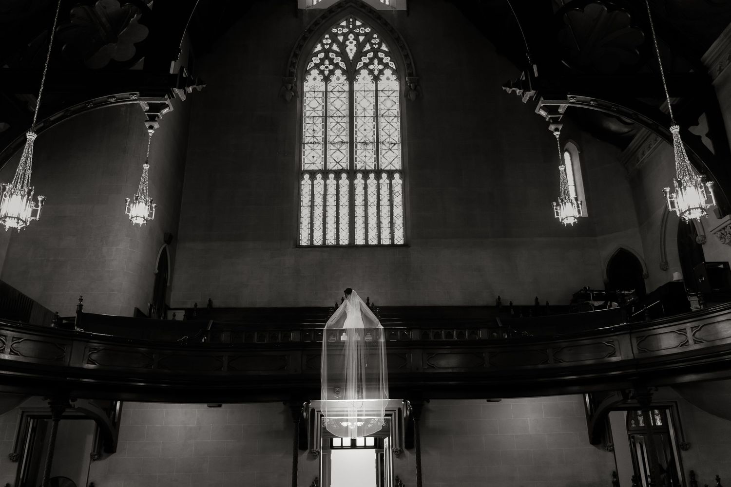 A dramatic black and white photo of an empty church interior with gothic windows and hanging lights.