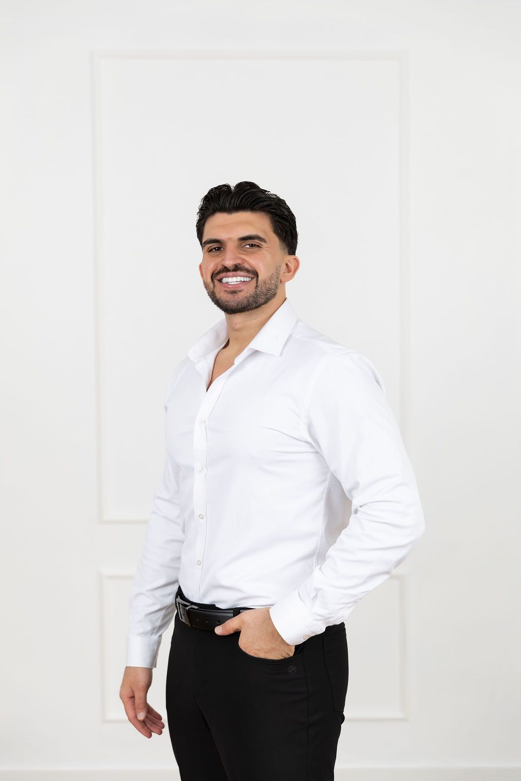 A person wearing a crisp white button-down shirt and black pants poses against a white background.