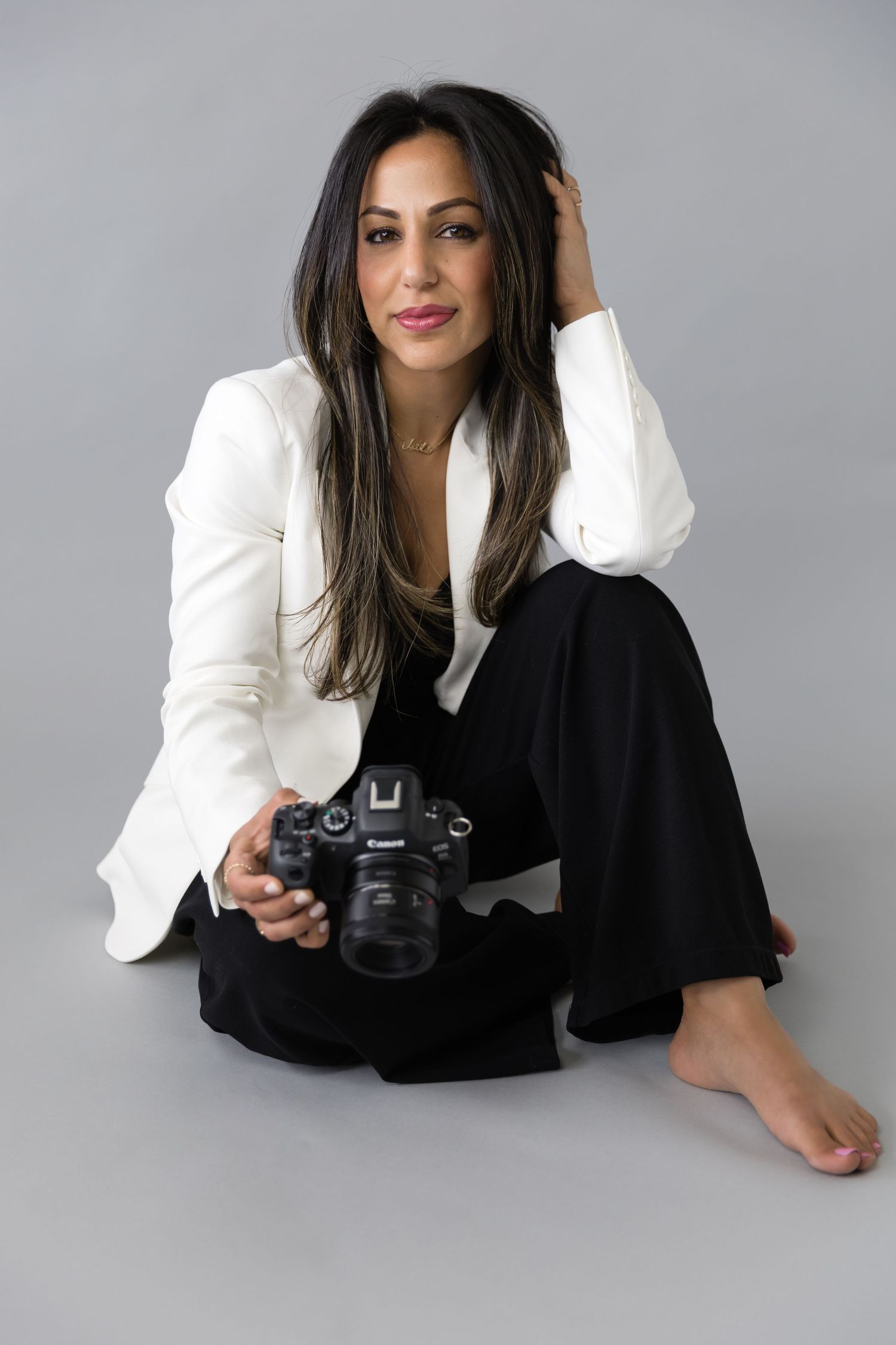 Elegant portrait of photographer in white blazer holding camera on gray backdrop.
