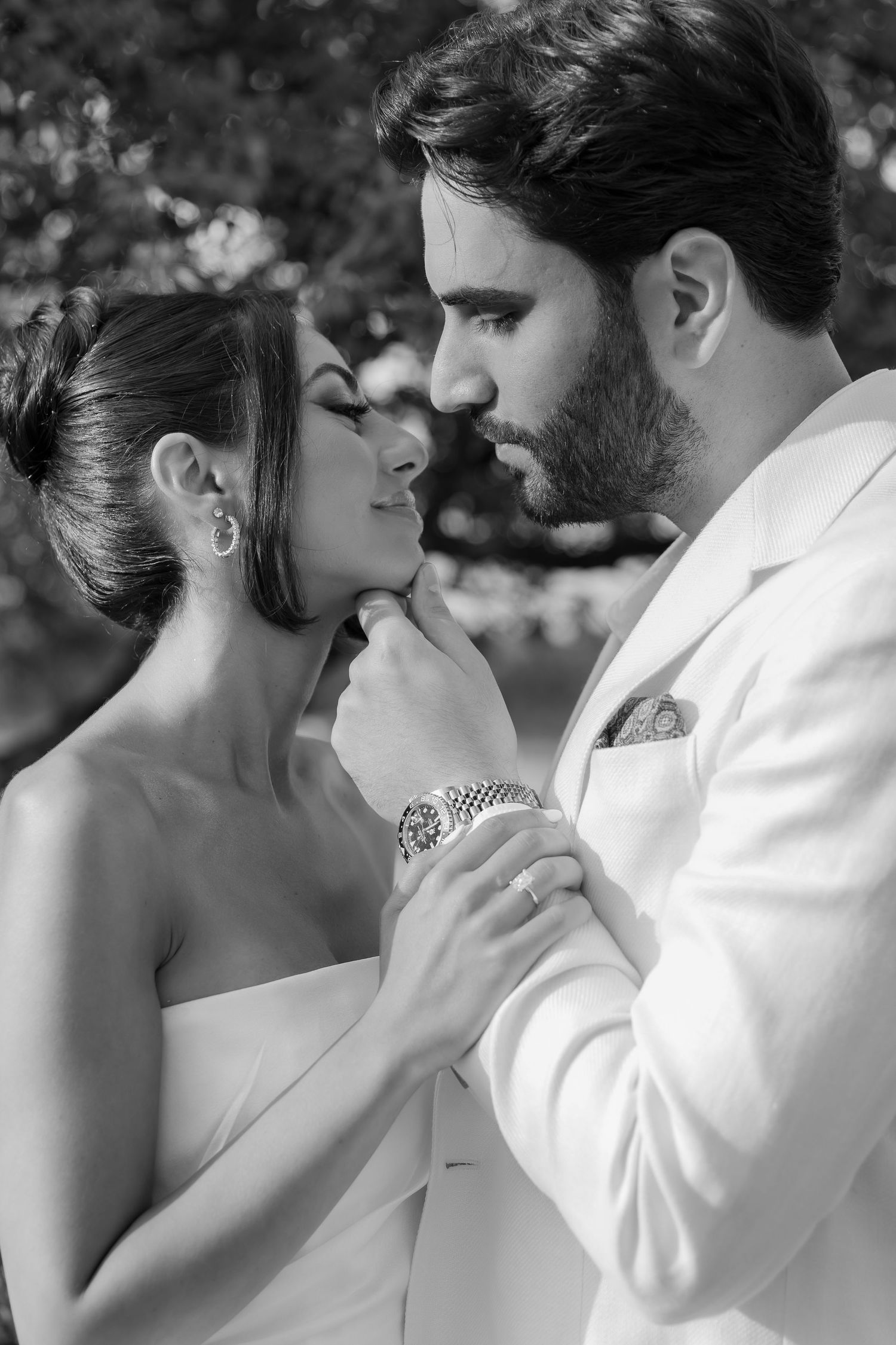 An intimate black and white portrait of a couple in formal attire sharing a tender moment.