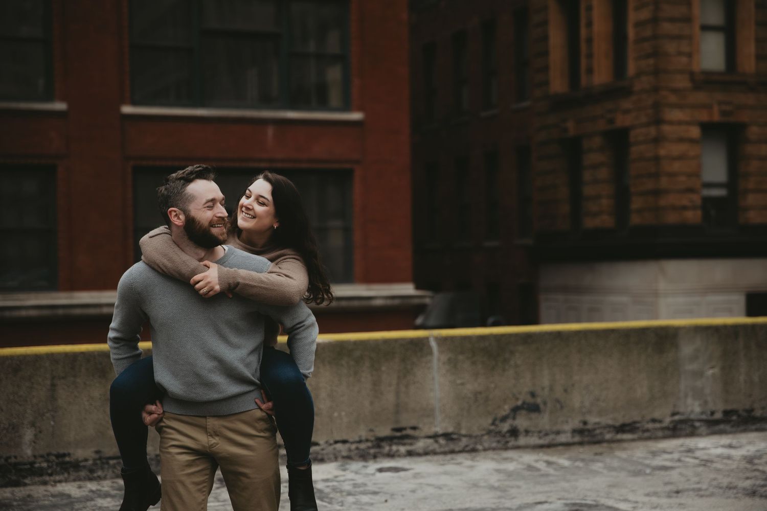 A couple sharing an intimate embrace against a brick building backdrop in an urban setting.