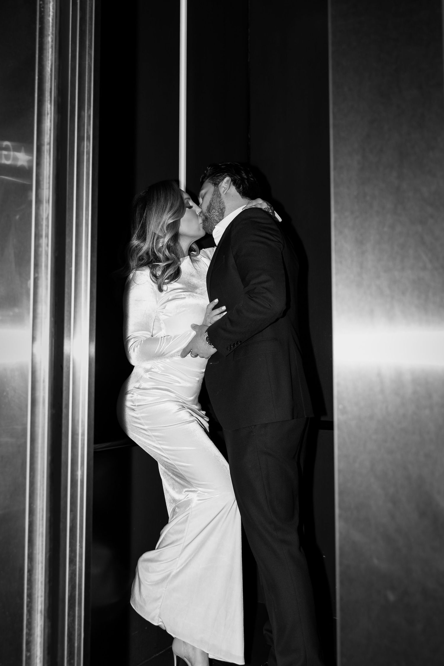 Intimate black and white photo of newlyweds sharing a romantic moment against a wall.