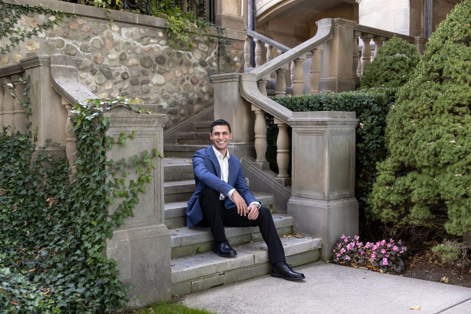 Man in blue suit sitting on stone steps surrounded by ivy and architecture.