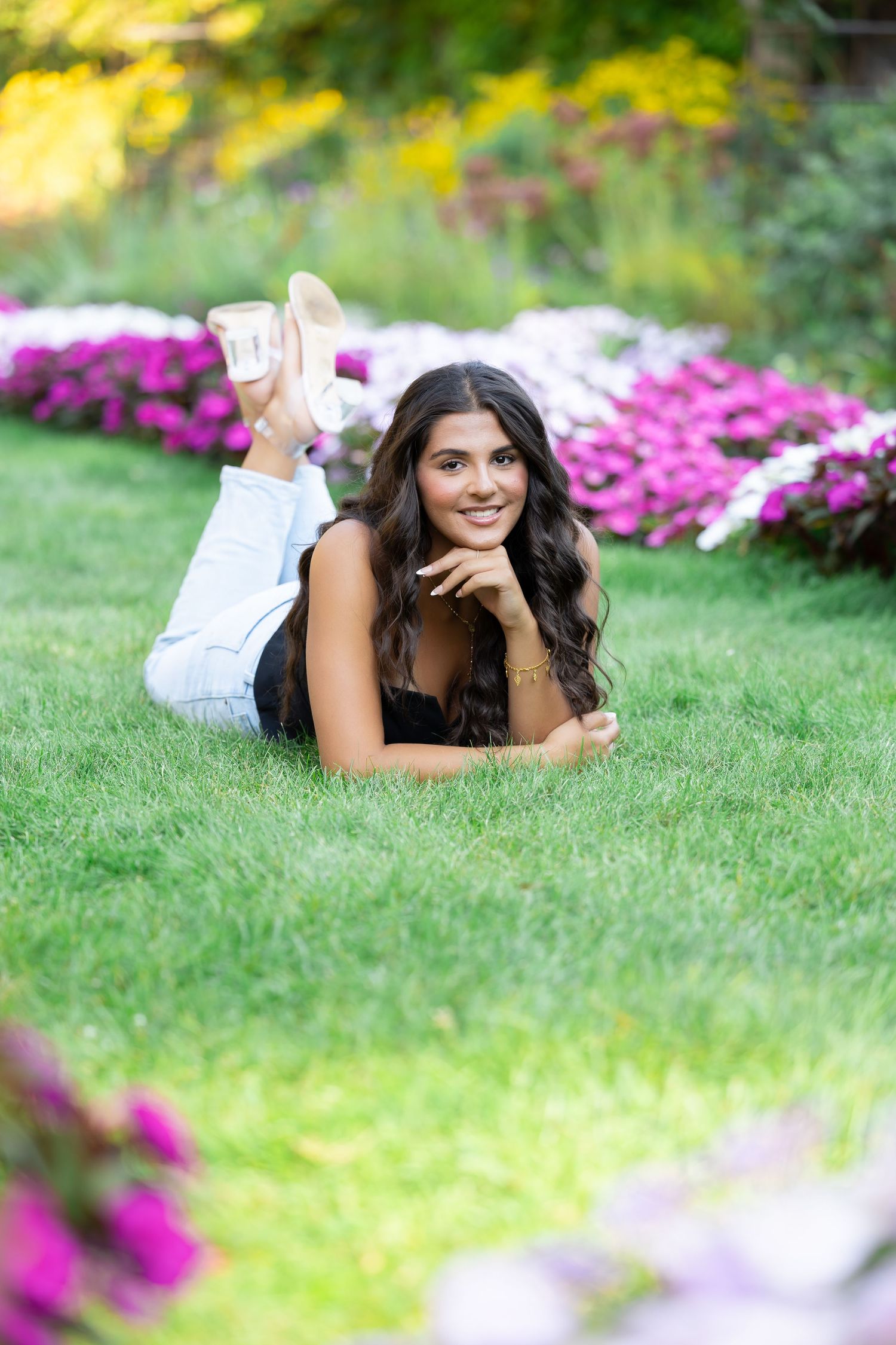Woman lying on grass near bright pink flowers in casual outdoor photo.