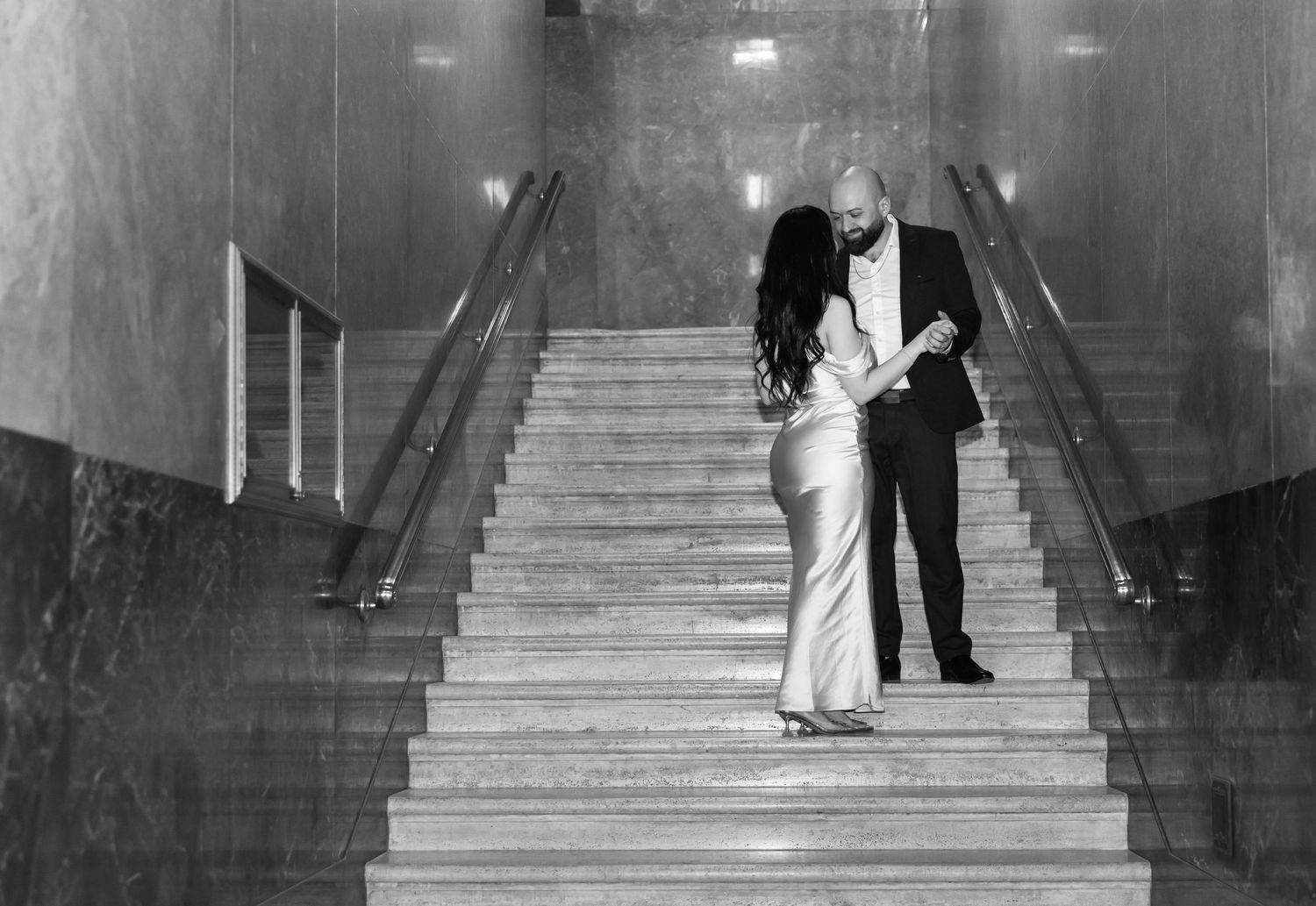 A couple embracing on elegant marble stairs in a classic black and white photograph.