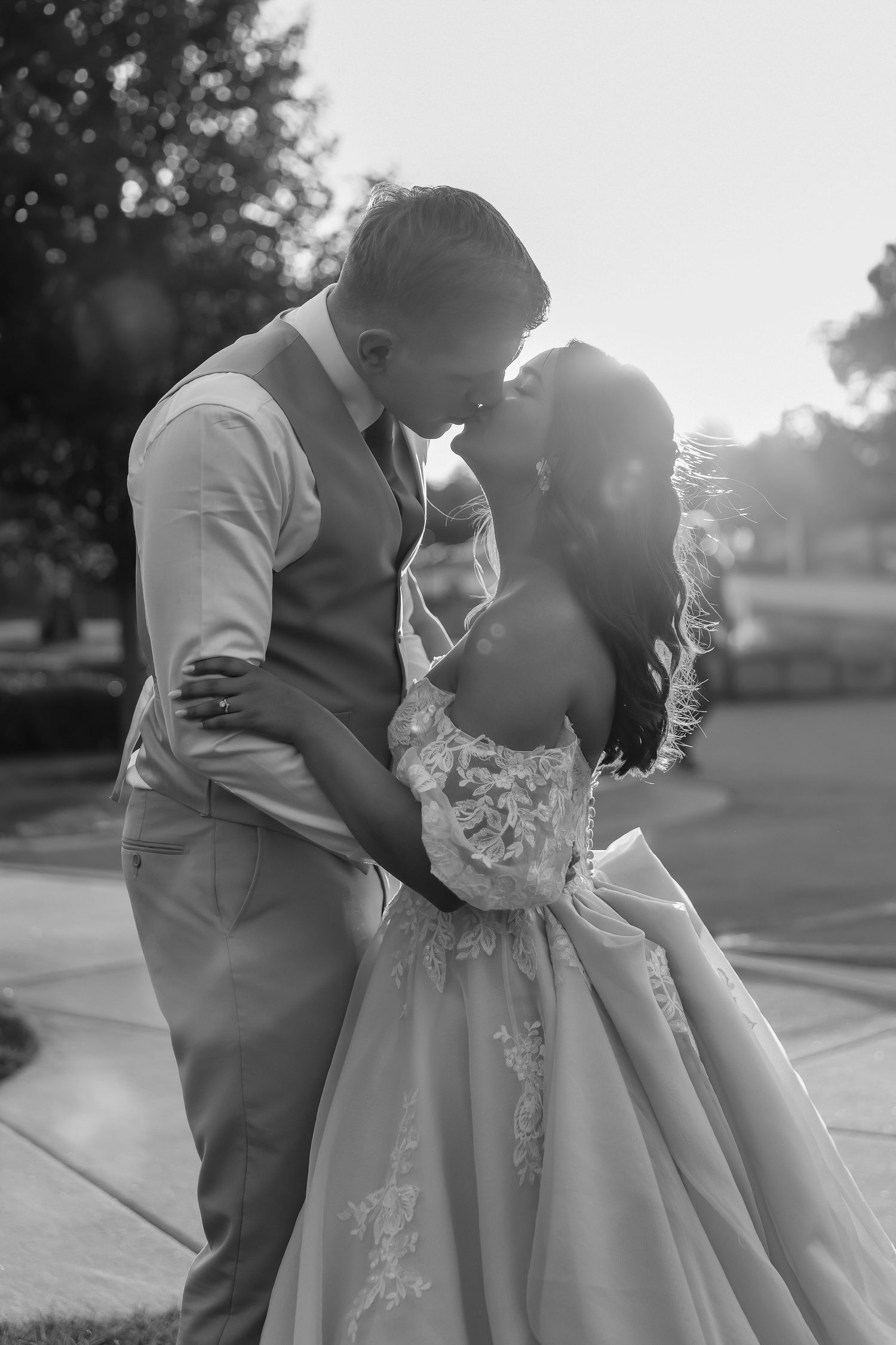 A tender black and white portrait of a couple in wedding attire sharing an intimate moment outdoors.