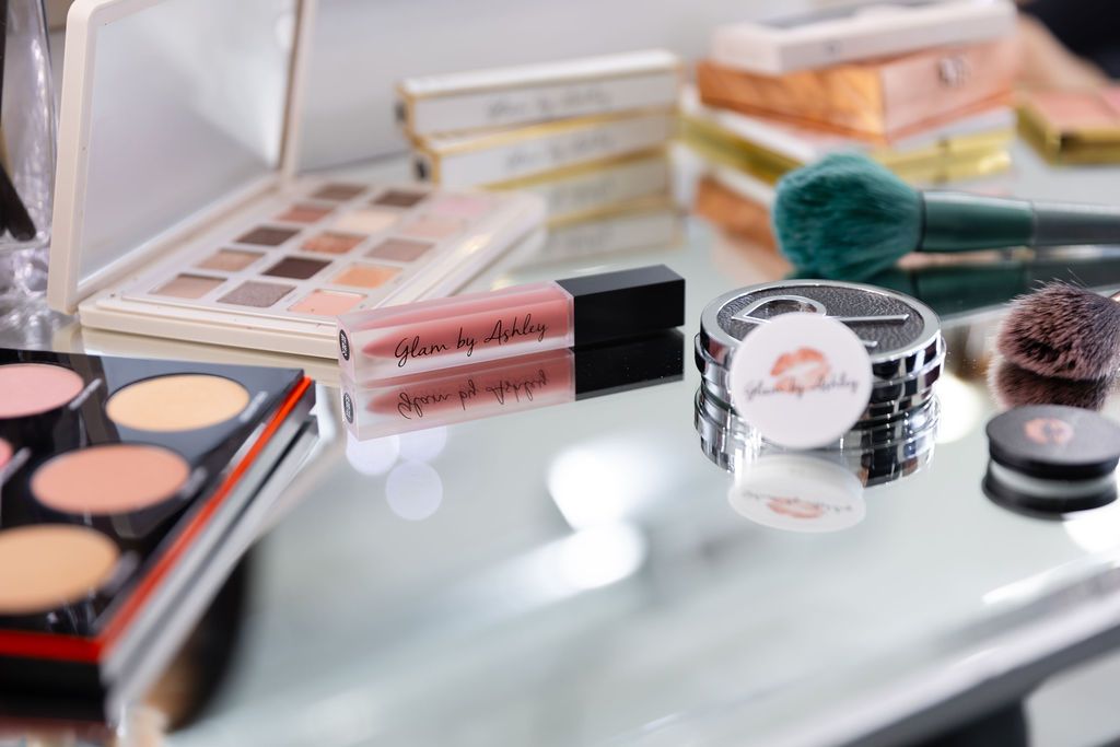 Various makeup products including eyeshadow palettes, lip gloss, and cosmetic brushes arranged on a light surface.