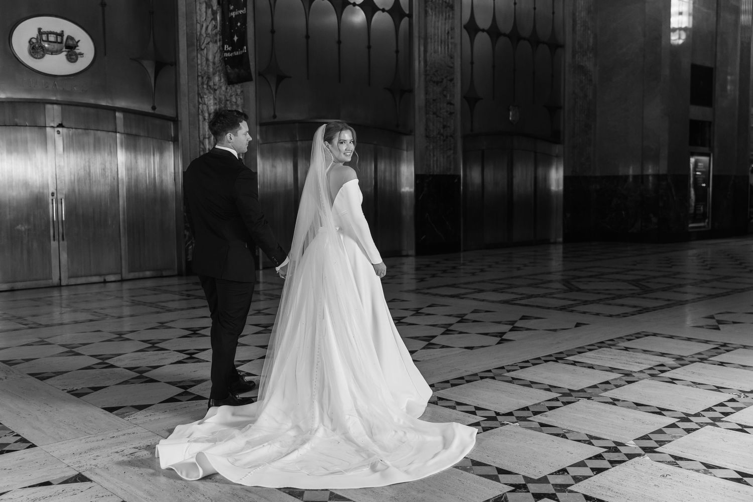 A black and white wedding photo showcasing a long flowing train on a patterned floor.