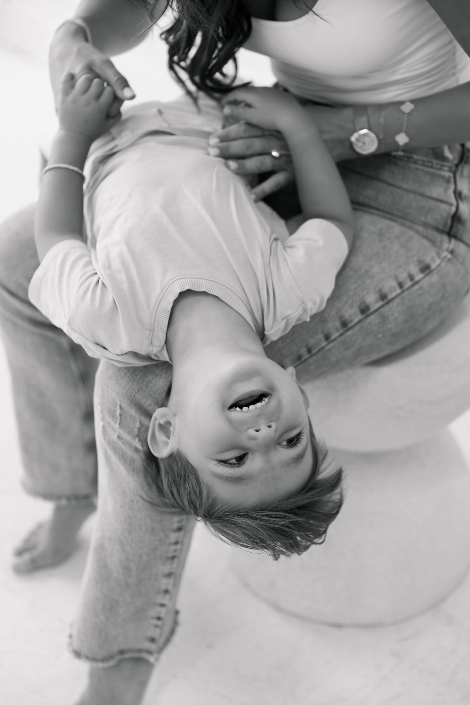 Black and white photo of a child playing upside down with a caregiver in casual denim, laughing joyfully.