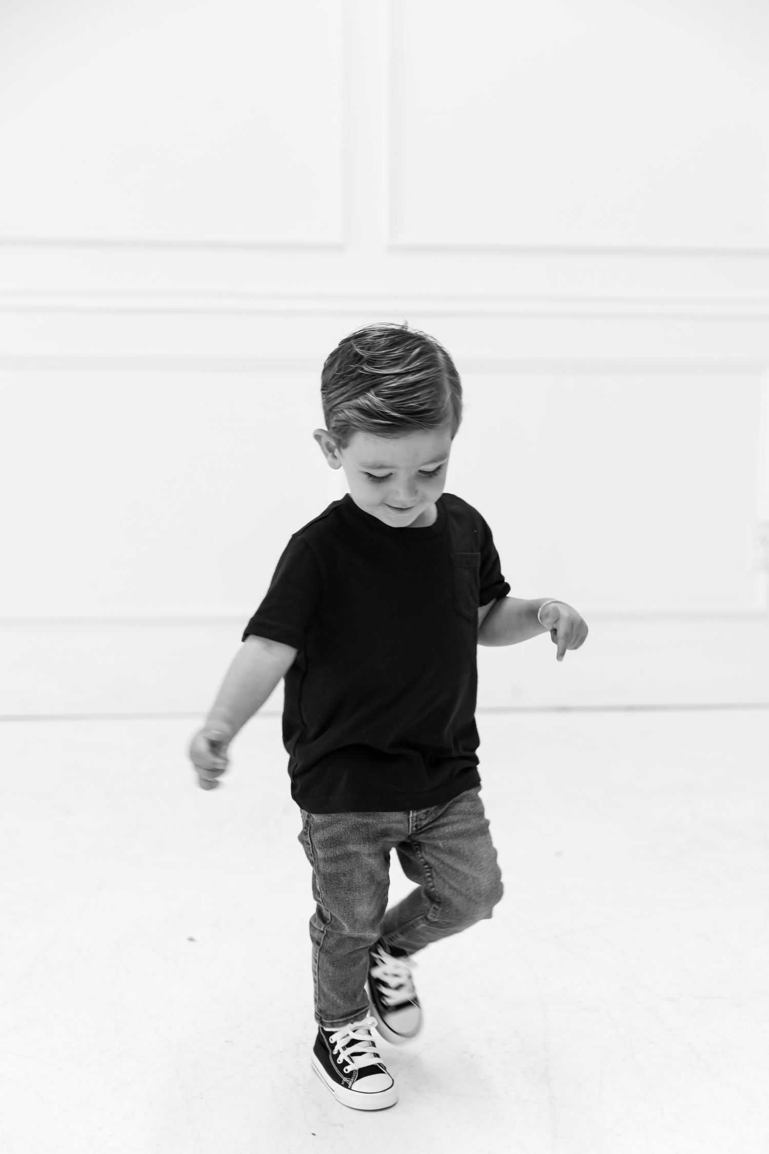 Black and white portrait of a child in a black t-shirt and jeans dancing against a white wall.