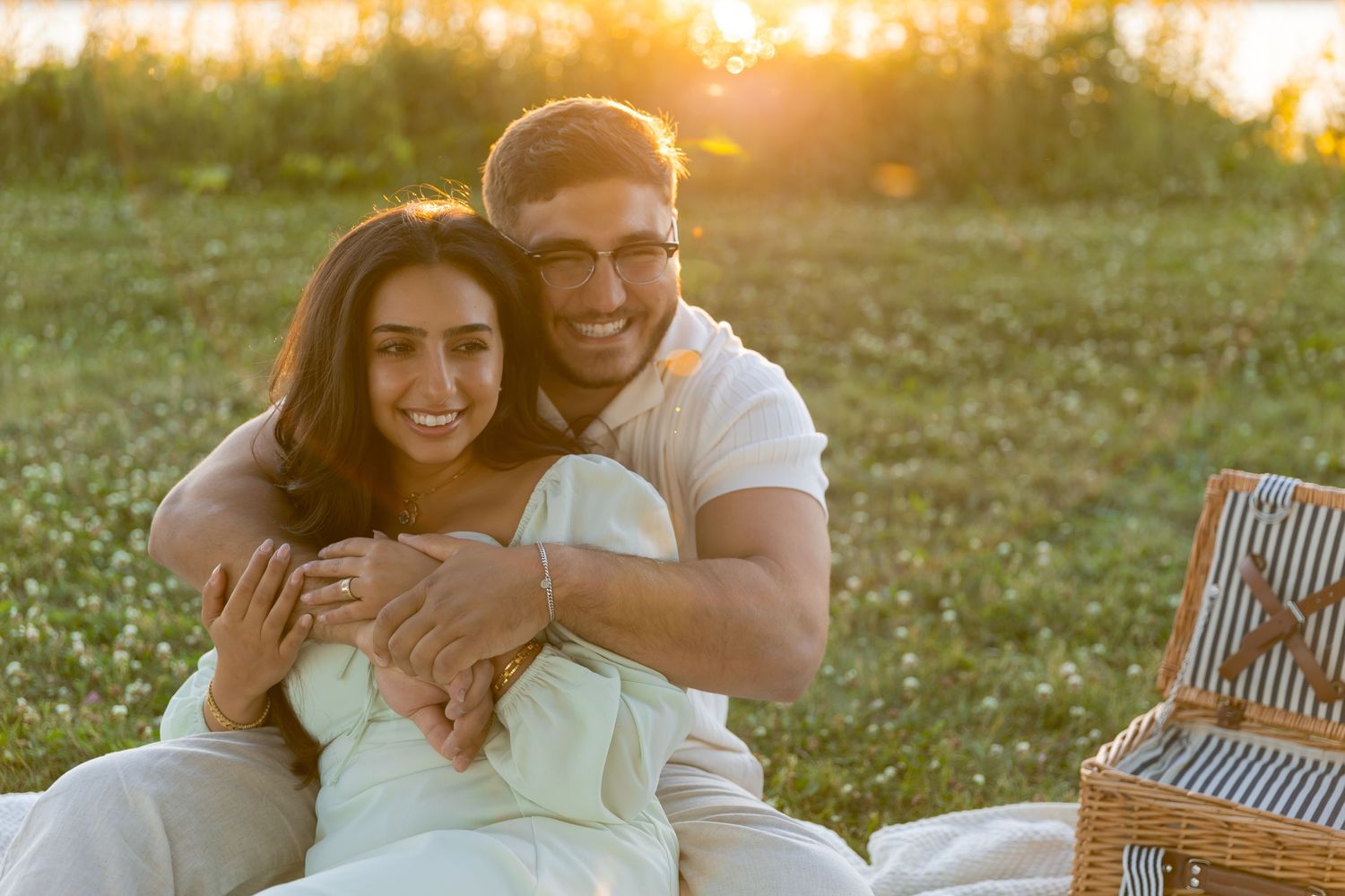 Couple embracing on picnic blanket during golden hour in parkland setting.