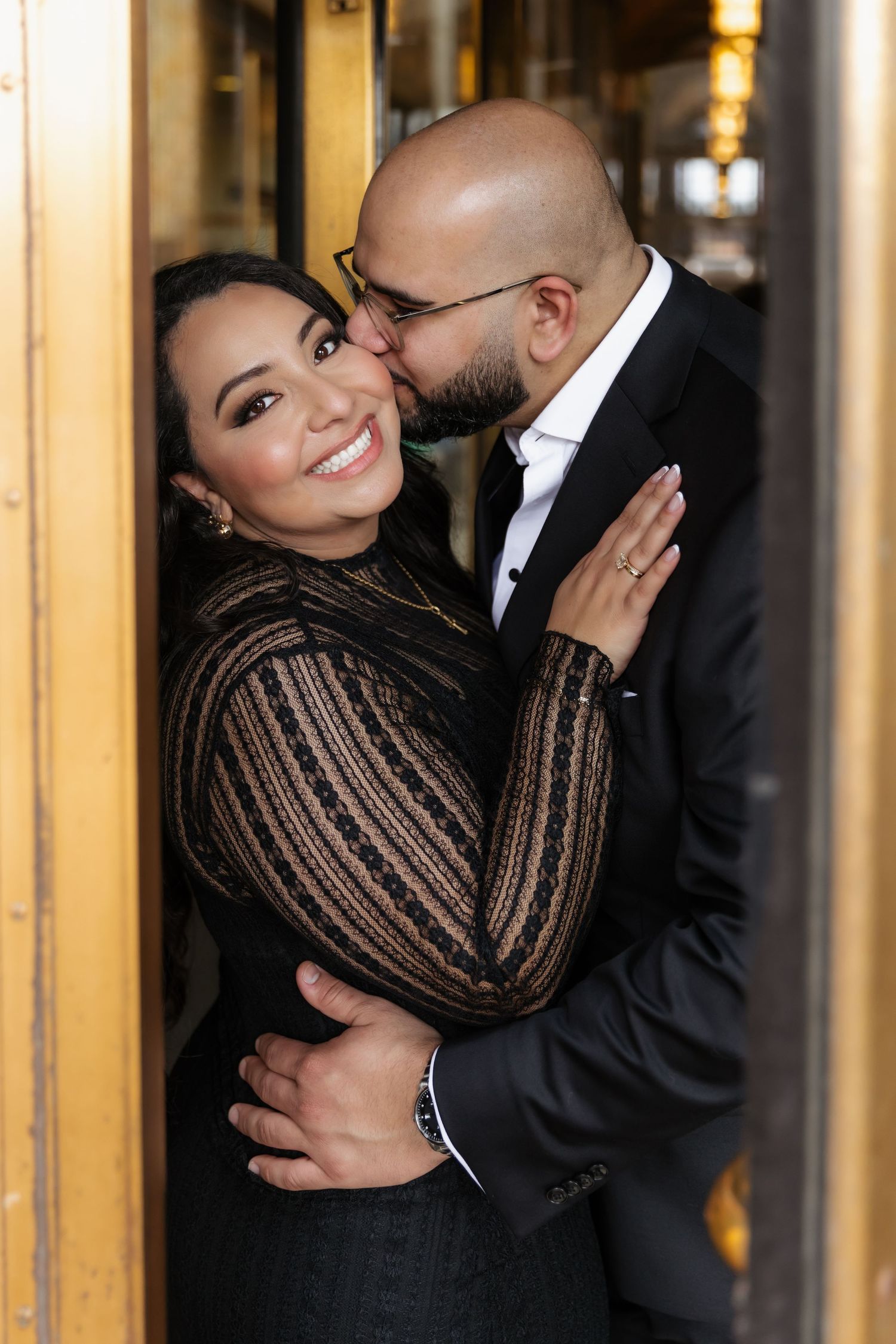 A couple shares an intimate moment in formal wear by golden doorway.