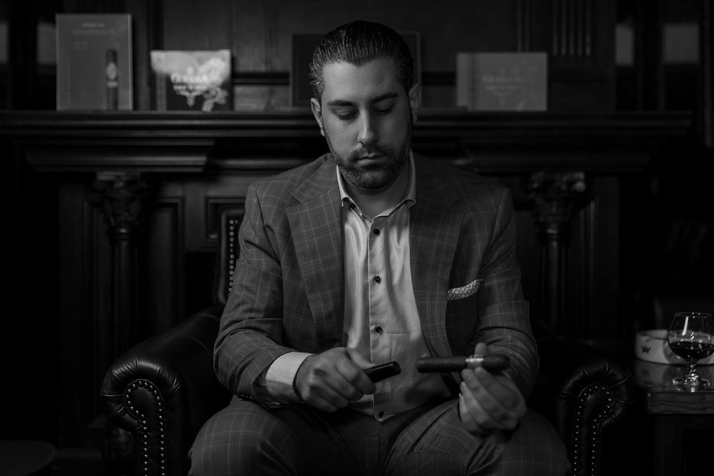 A person in a suit sits contemplatively in a leather armchair, captured in dramatic black and white lighting.