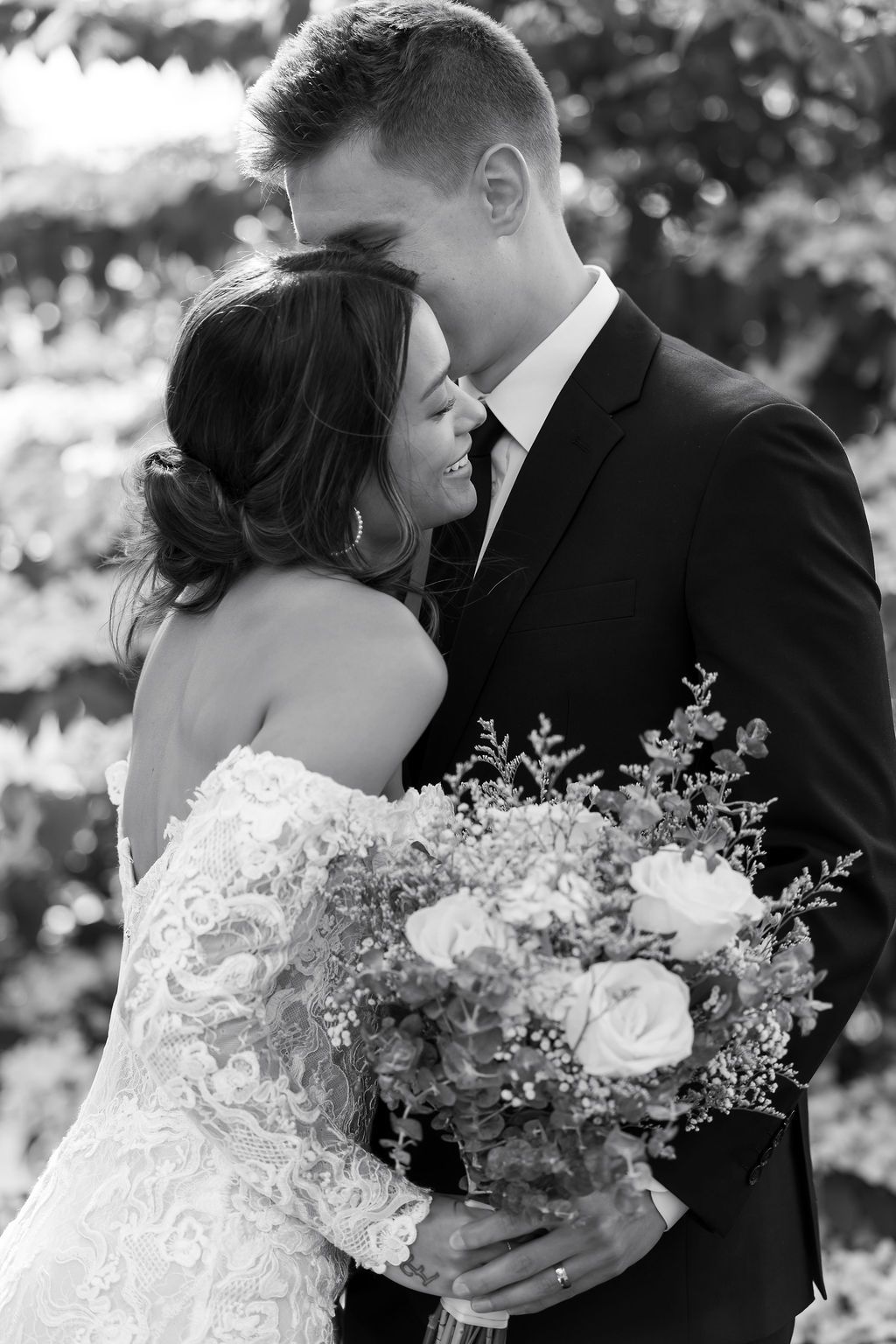 A tender black and white moment between newlyweds with the bride holding a romantic floral bouquet.