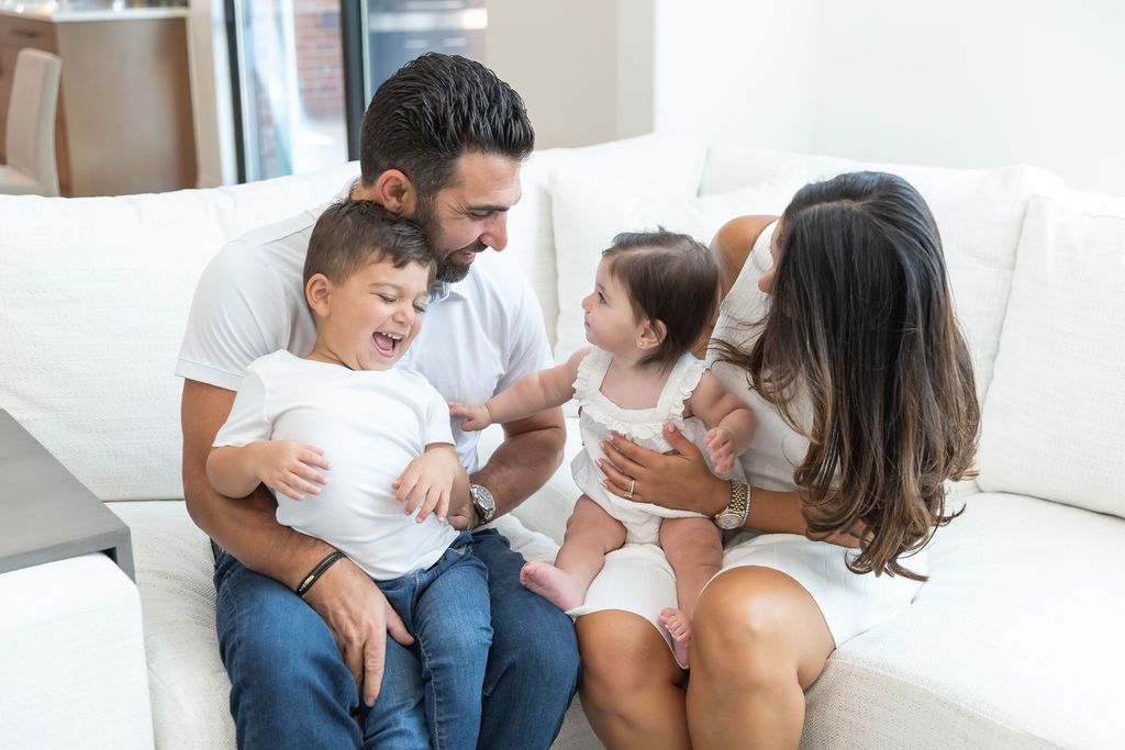 A family spending quality time together while sitting and laughing on a white couch in their living room.