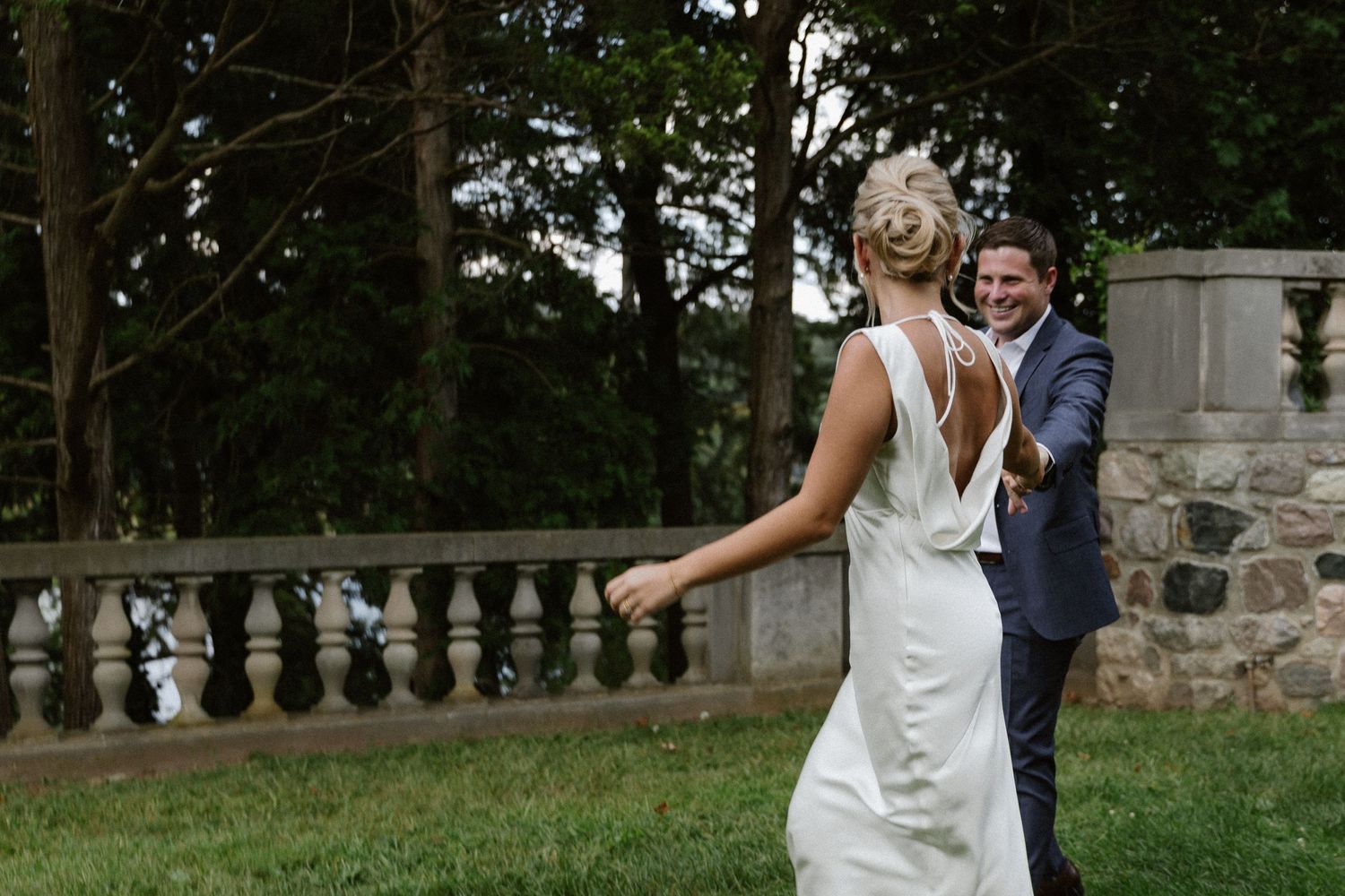 Wedding couple sharing joyful moment on outdoor stone terrace surrounded by trees.