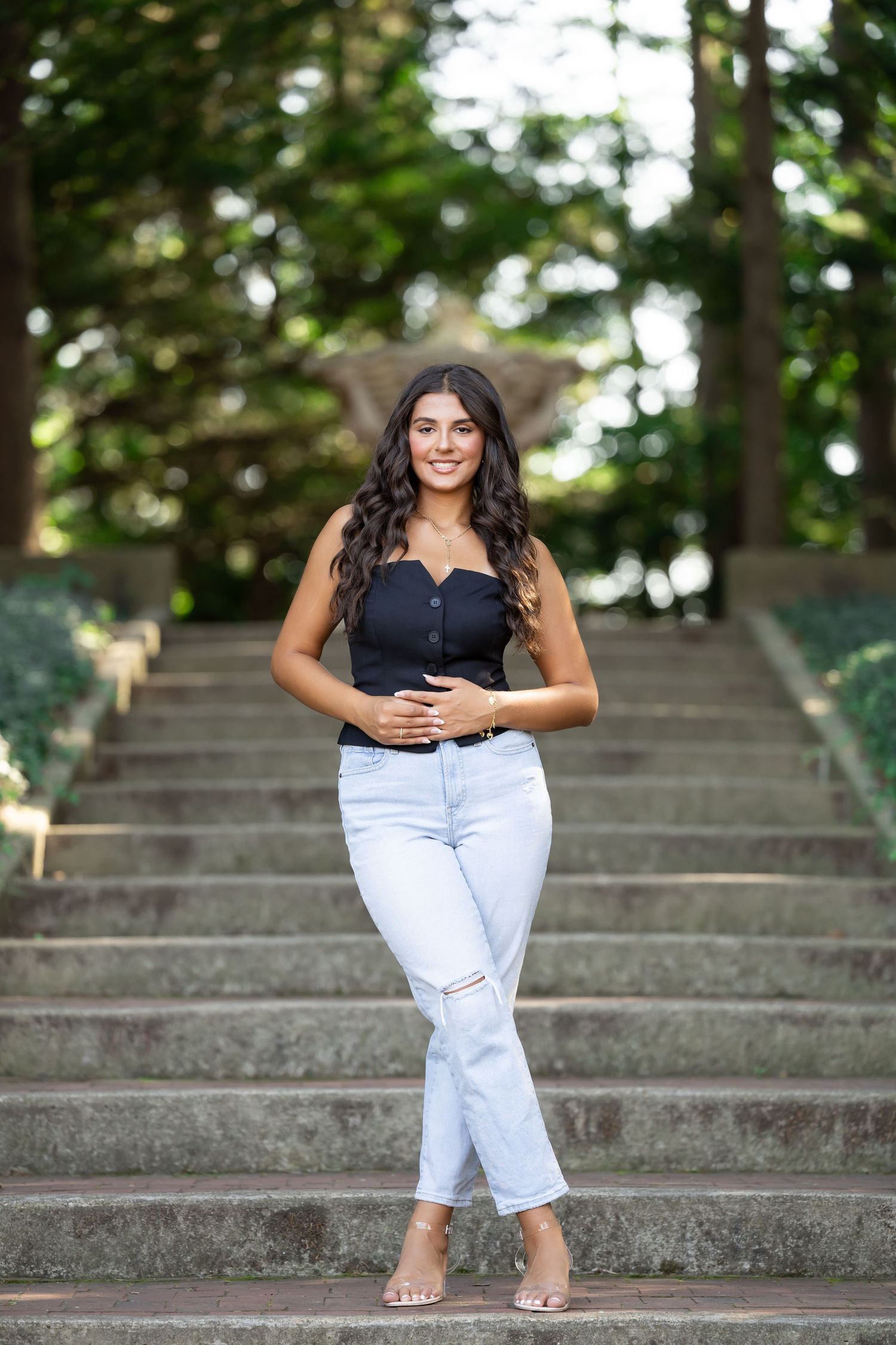 Woman wearing black top and light jeans stands casually on outdoor stone steps.
