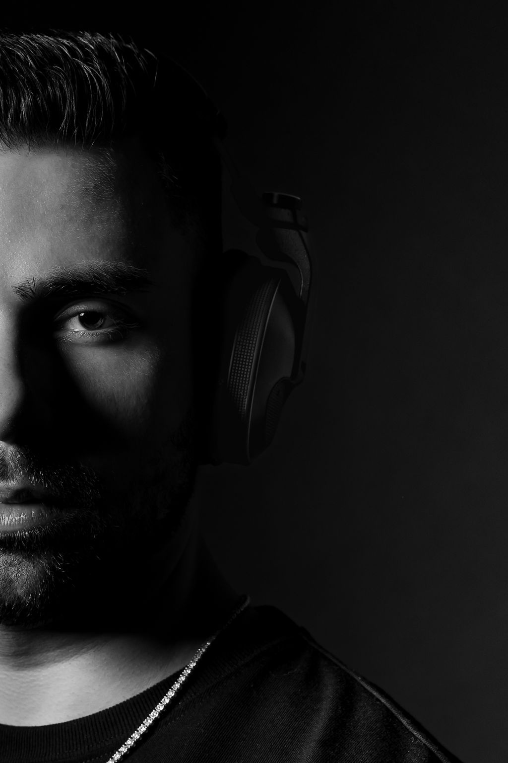 Professional black and white studio portrait of musician wearing headphones in dramatic lighting.