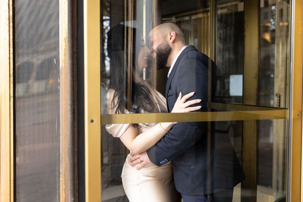 A loving moment captured between a couple in a revolving glass door entrance.