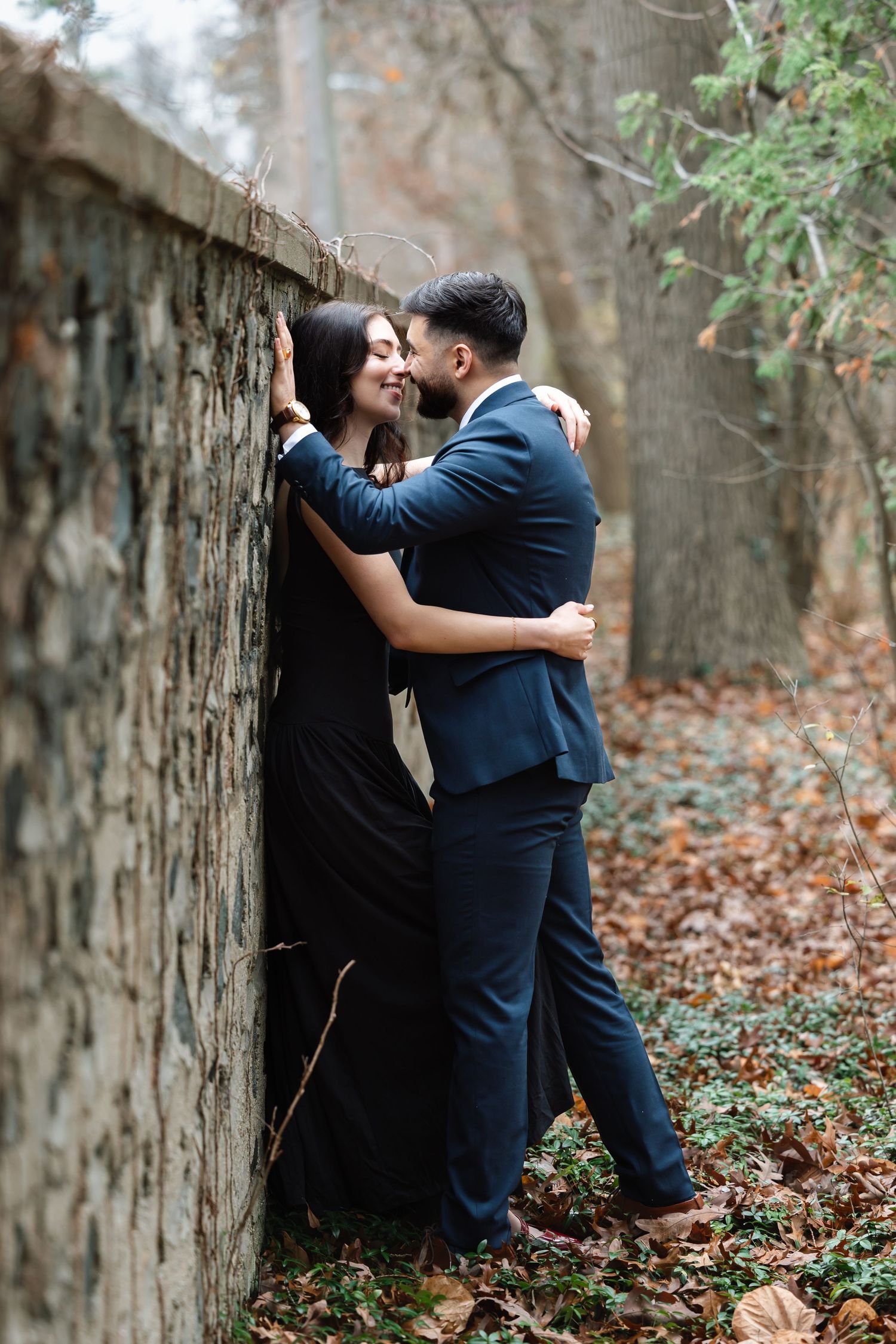 Romantic couple embracing against stone wall in autumn forest setting.