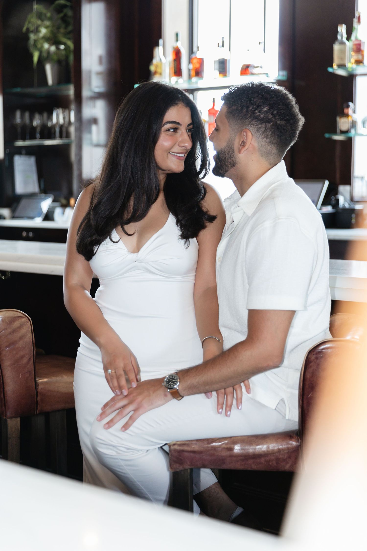 Stylish couple in white attire sharing romantic moment at upscale bar setting.