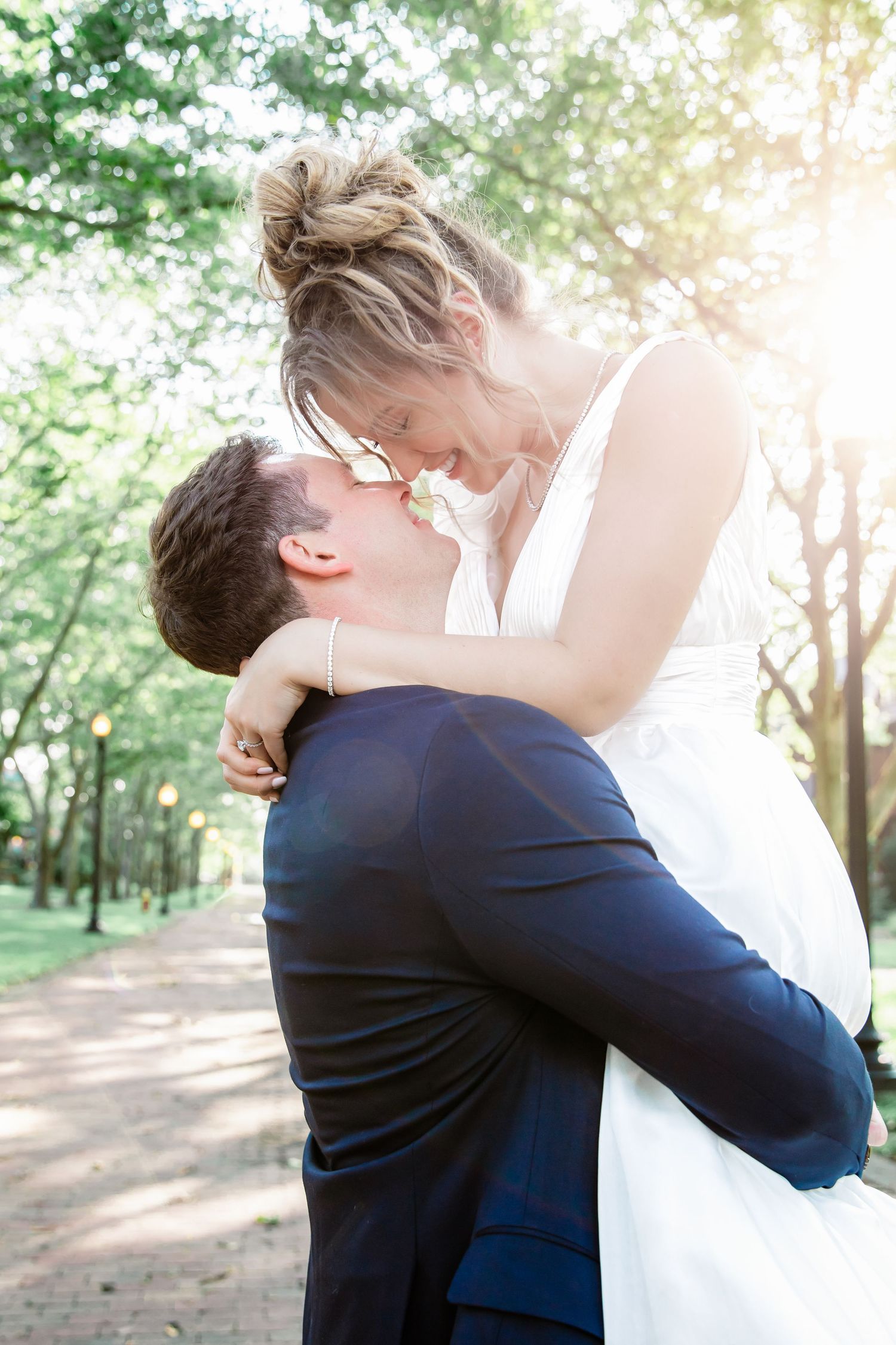 A sun-drenched romantic moment between newlyweds on a tree-lined path.