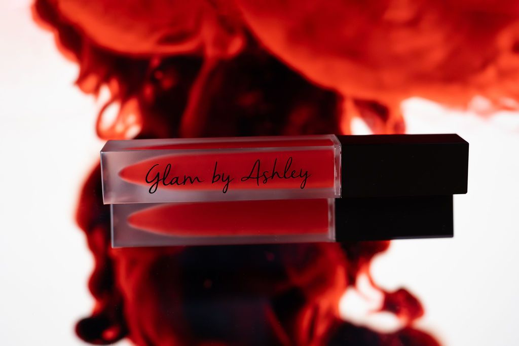 Red glass lip gloss container on dark background with dramatic red smoke effects behind it.