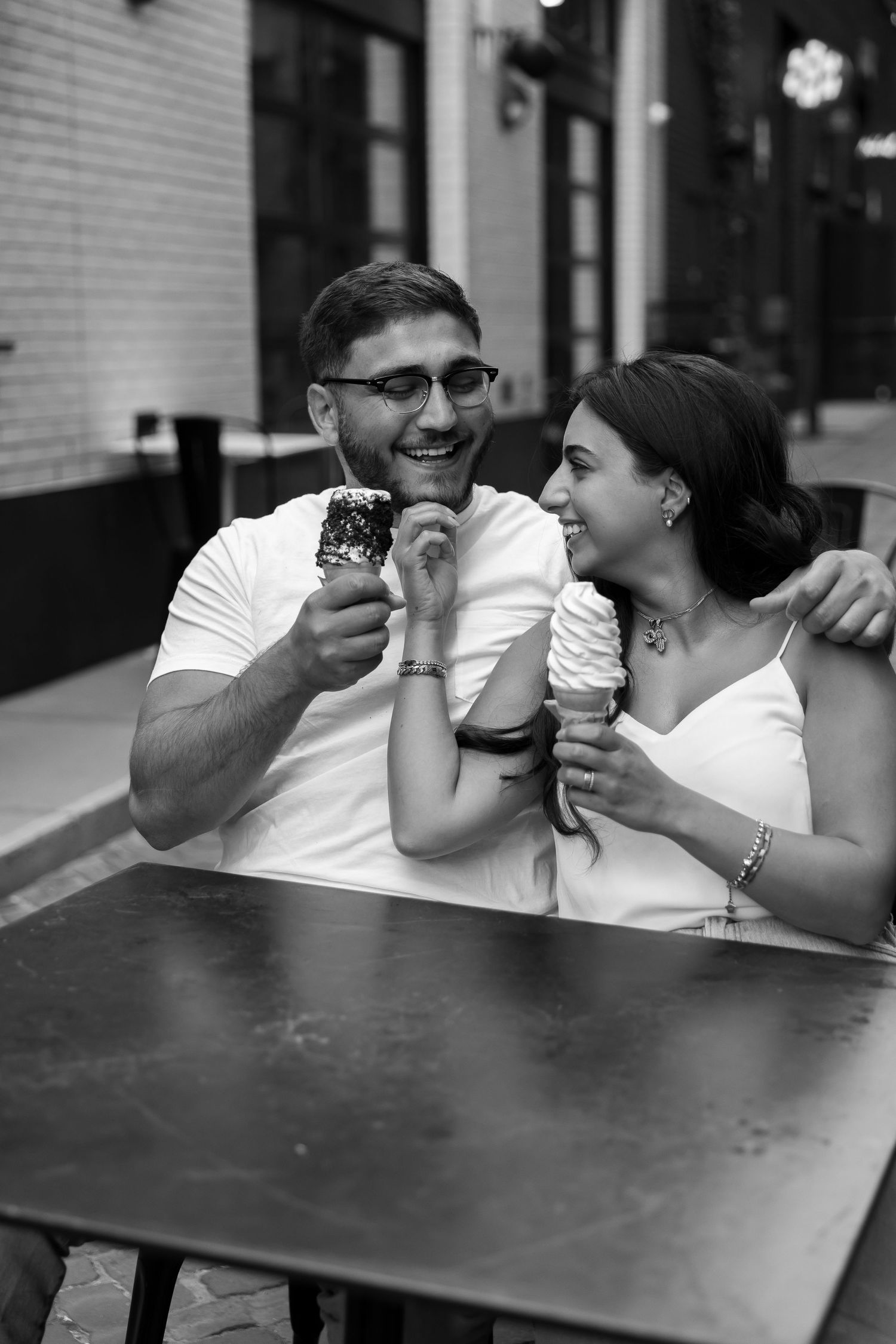 Couple enjoying ice cream together while sitting at an outdoor table, sharing a lighthearted moment.